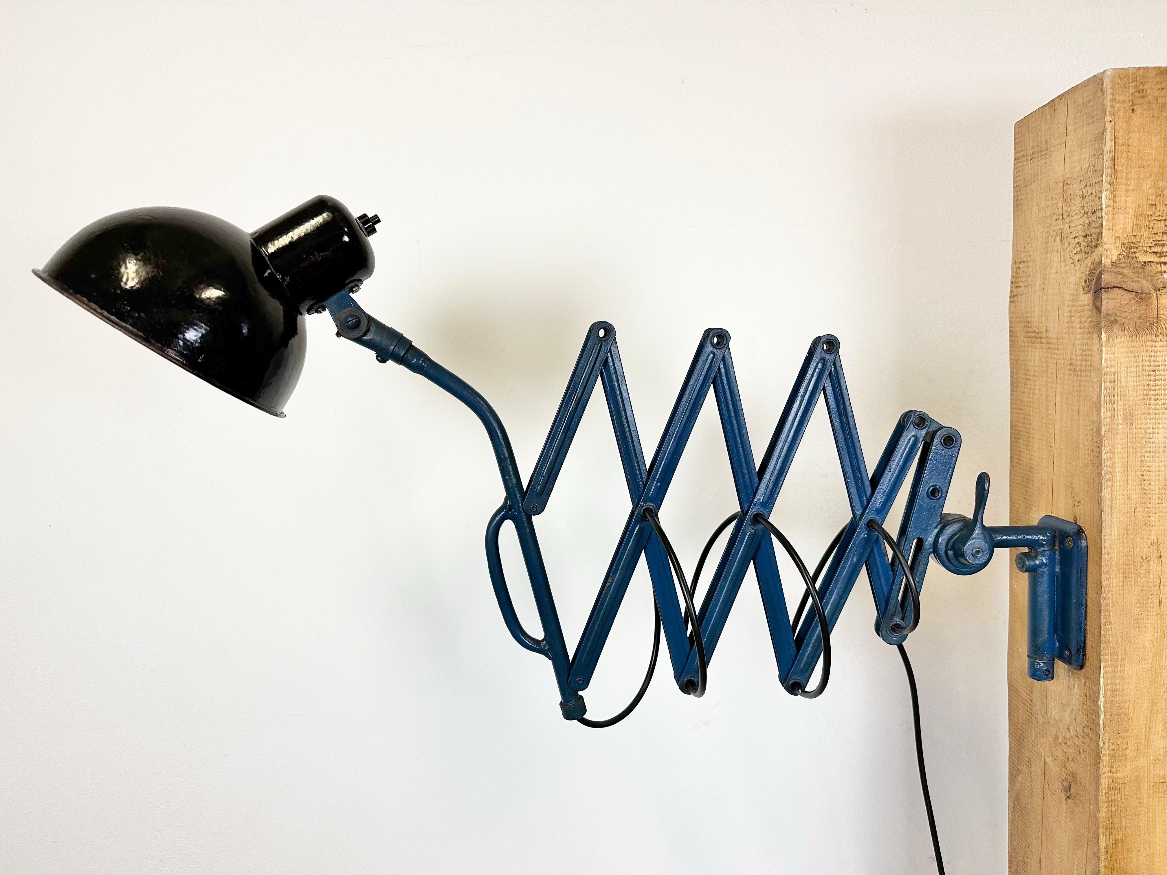 This vintage Industrial scissor lamp was produced in former Czechoslovakia during the 1930s. The lamp has a black enamel metal shade with white enamel interior. Blue iron scissor arm is extendable and can be turned sideways. New porcelain socket