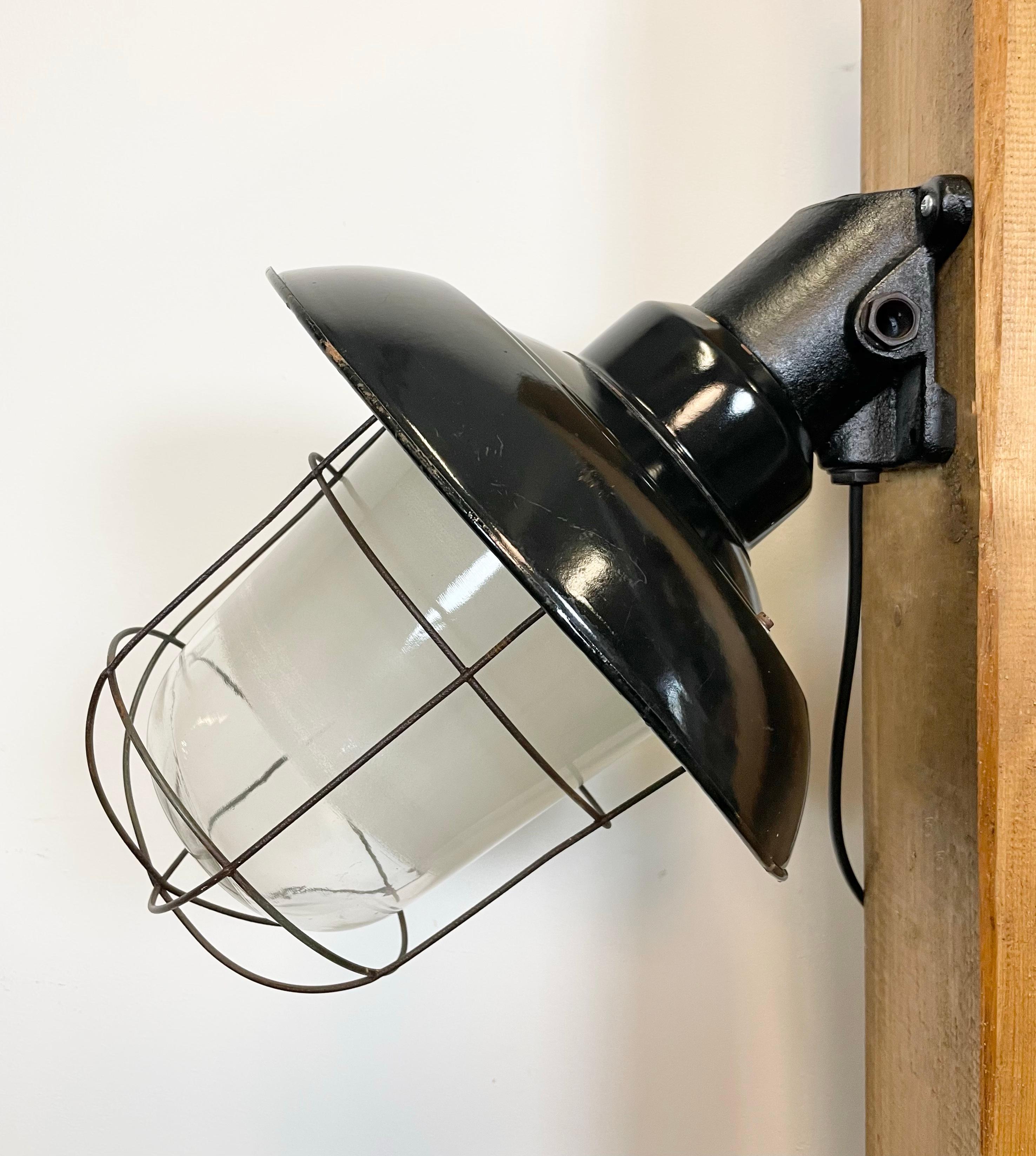 - Industrial wall lamp with cast iron wall mouting from former Czechoslovakia made during the 1960s
- Black enamel shade with white enamel interior, glass cover, iron grid
- New porcelain socket for E 27 light bulbs and wire
- Weight: 5 kg.
