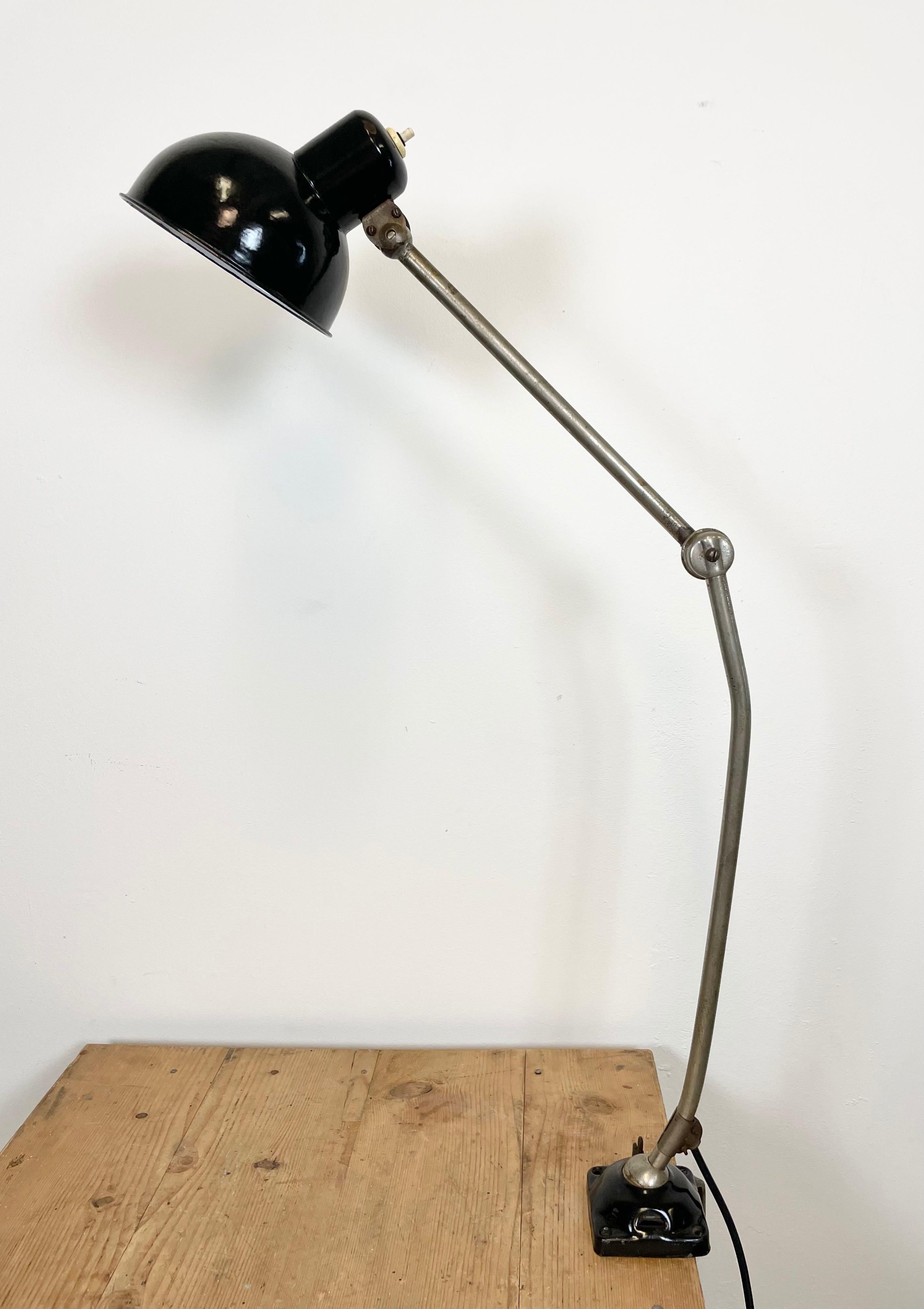 Industrial table lamp made in former Czechoslovakia during the 1950s.It features a black enamel shade with white interior, an iron base and arm with three adjustable joints. The switch is situated directly on the lampshade.Original bakelite socket