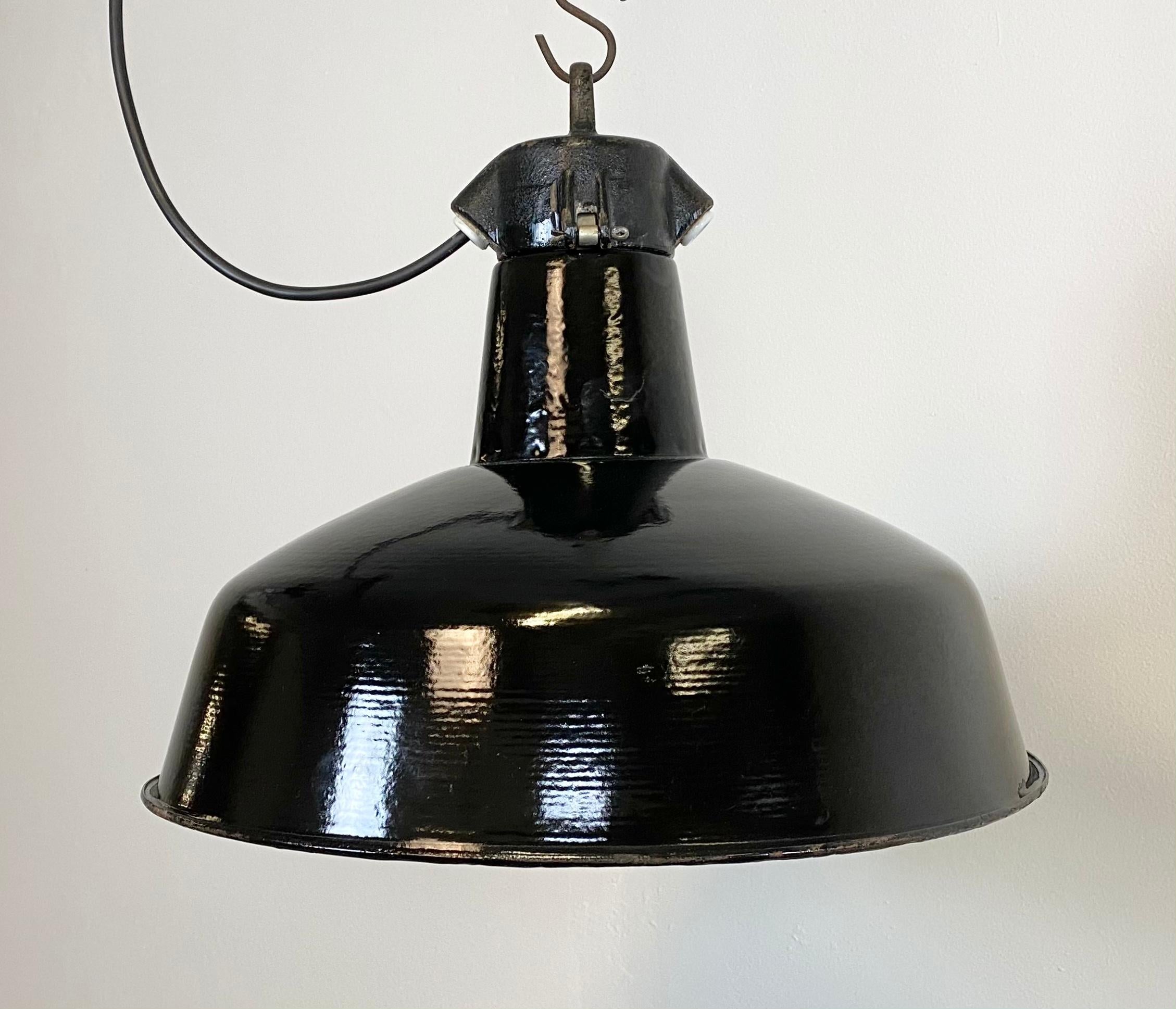 Industrial hanging light manufactured in former Czechoslovakia during the 1950s. It features a black enamel shade with white enamel interior and cast iron top. Porcelain socket for E 27 light bulbs and new wire. The weight of the lamp is 2 kg. The
