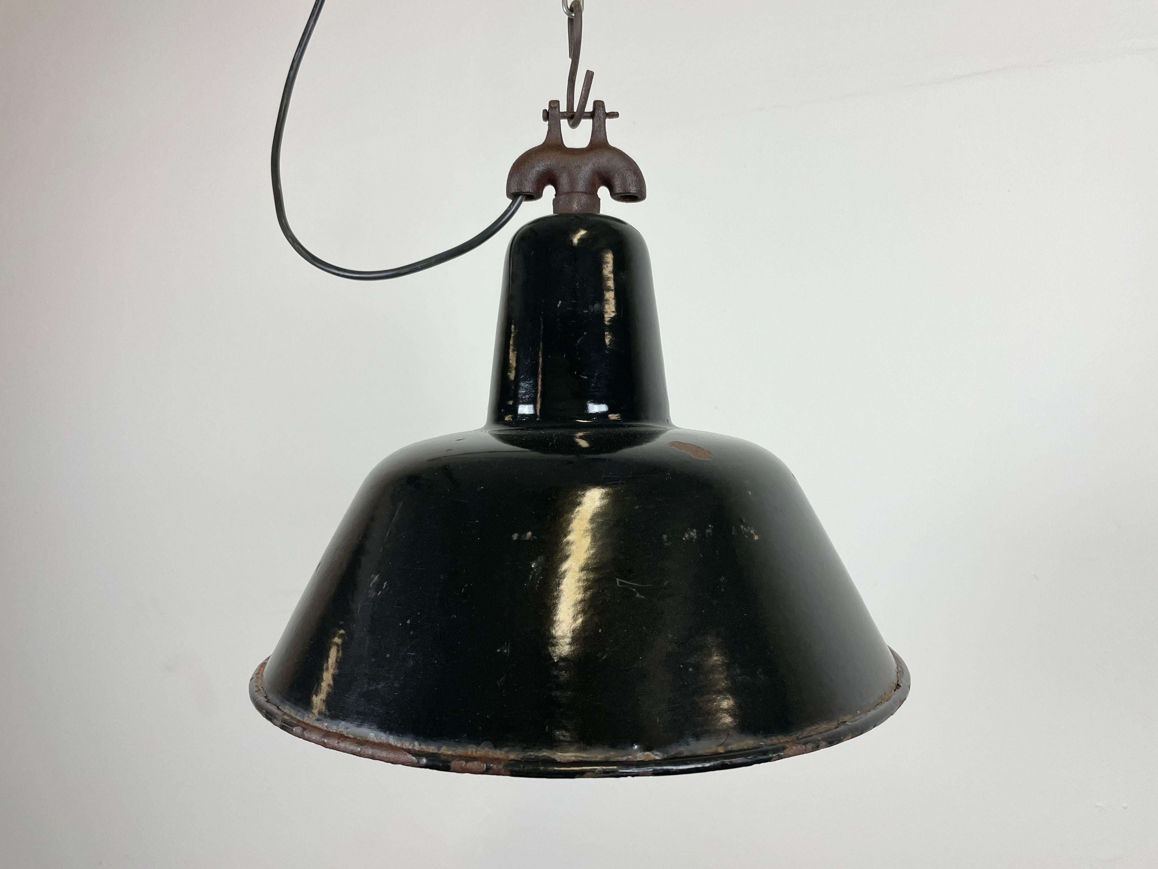 Industrial black enamel pendant light made in former Czechoslovakia during the 1950s. White enamel inside the shade. Cast iron top. The porcelain socket requires E 27 light bulbs. New wire. Fully functional. The weight of the lamp is 1 kg.