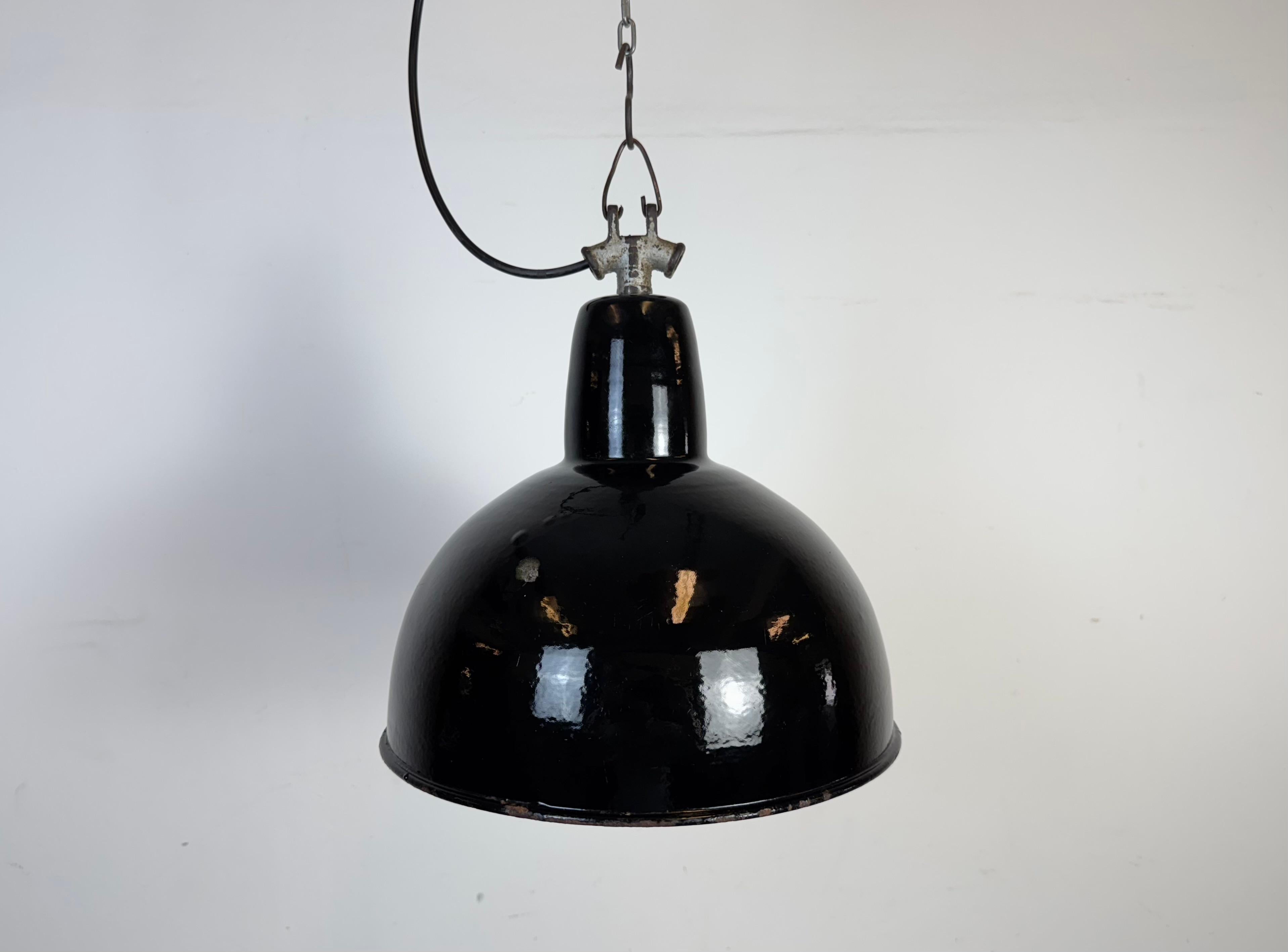 Suspension industrielle en émail noir fabriquée dans l'ancienne Tchécoslovaquie dans les années 1950. Émail blanc à l'intérieur de la teinte. Dessus en fonte. La douille en porcelaine est compatible avec les ampoules standard E 27/ E26. Un nouveau