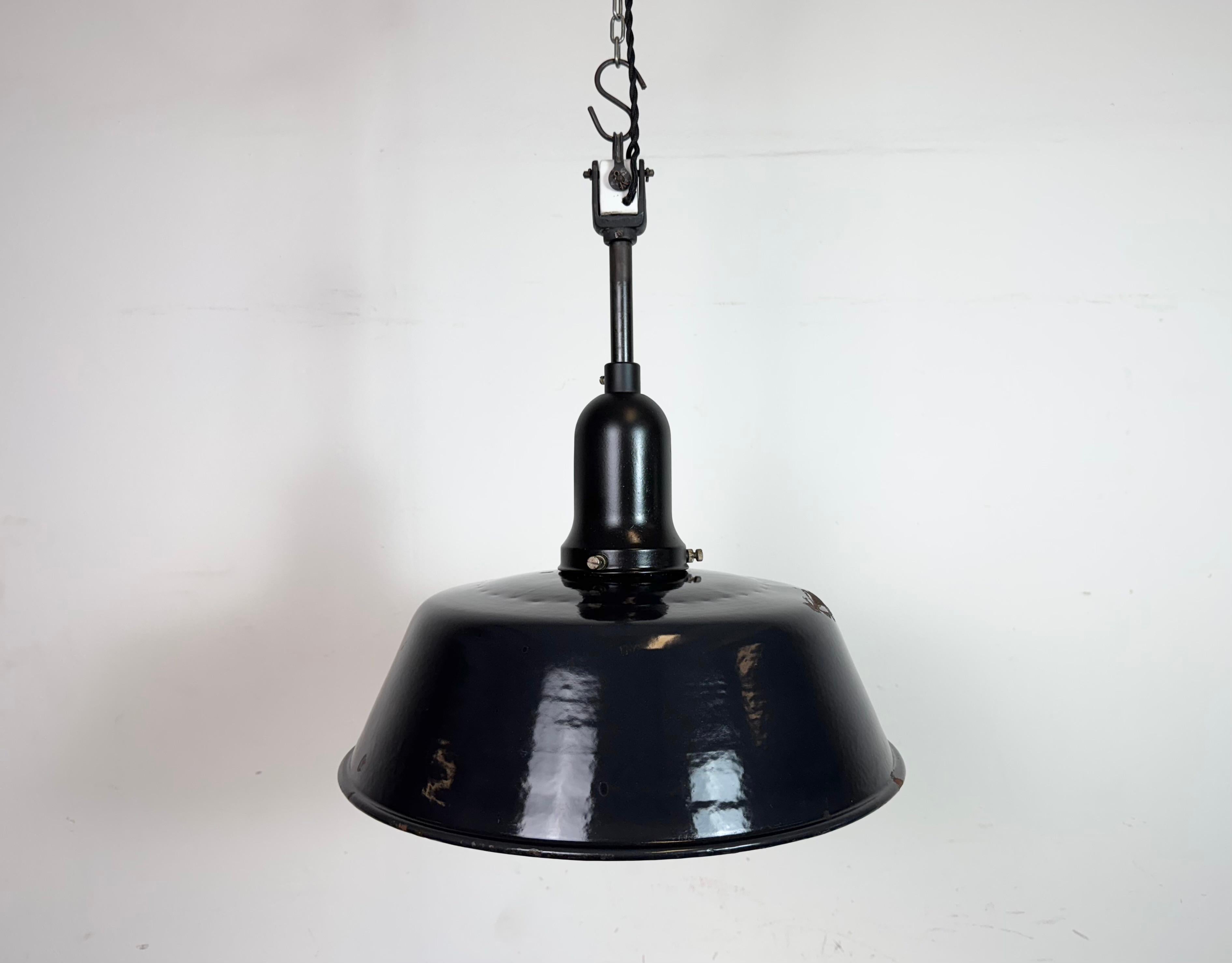 Suspension industrielle en émail noir fabriquée en Allemagne dans les années 1950. Émail blanc à l'intérieur de la teinte. Dessus en porcelaine. La douille est compatible avec les ampoules standard E27/ E26. Un nouveau fil. Entièrement fonctionnel.