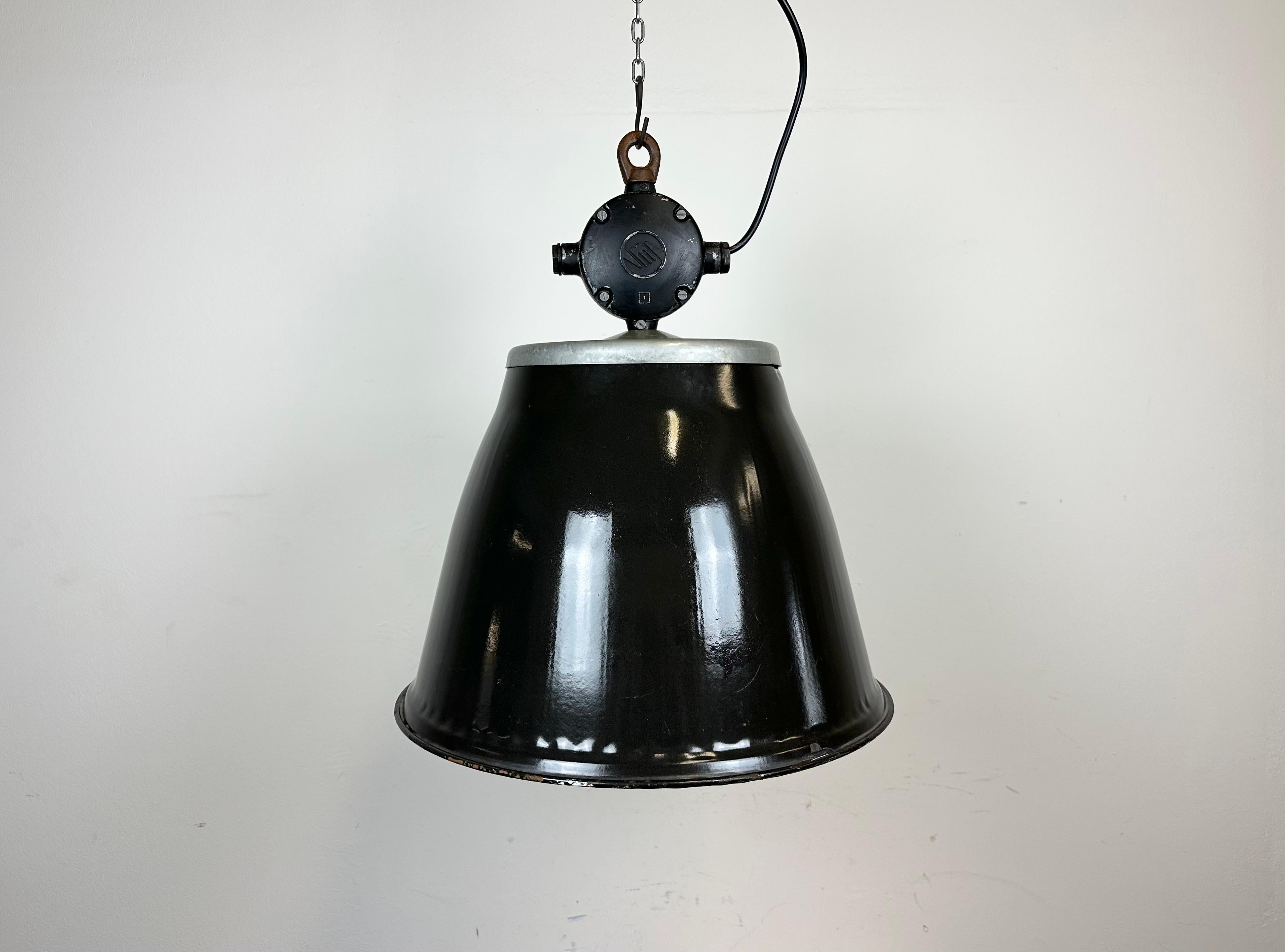 Lampada a sospensione industriale in smalto realizzata da Elektrosvit nell'ex Cecoslovacchia durante gli anni '60. Presenta un piano in alluminio fuso e un paralume in smalto nero con interno bianco. La nuova presa in porcellana richiede lampadine