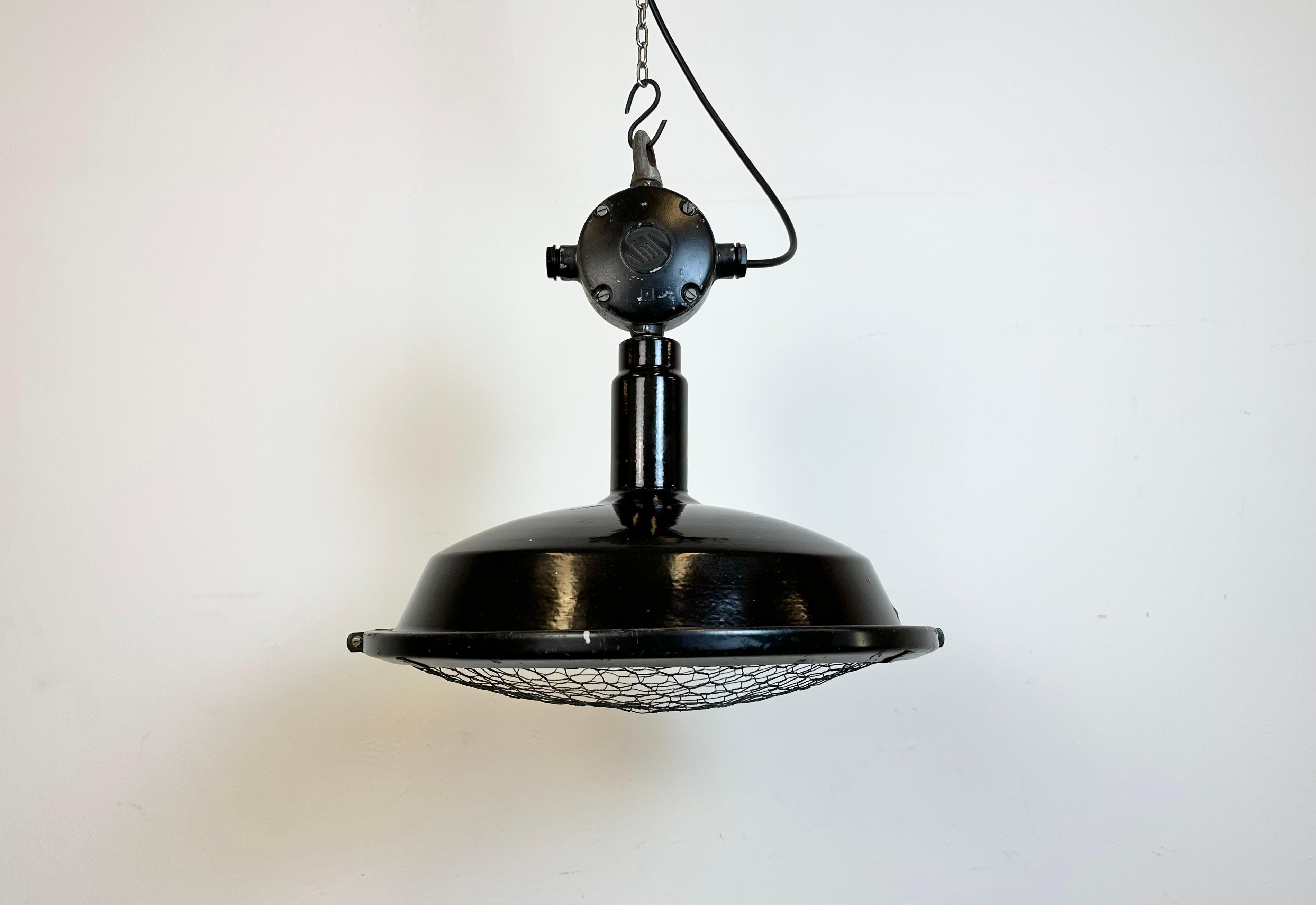 Industrial factory hanging lamp made by Elektrosvit in former Czechoslovakia during the 1950s. It features a black enamel shade with white enamel interior, a cast aluminium top box and an iron protective grid. New porcelain socket requires standard