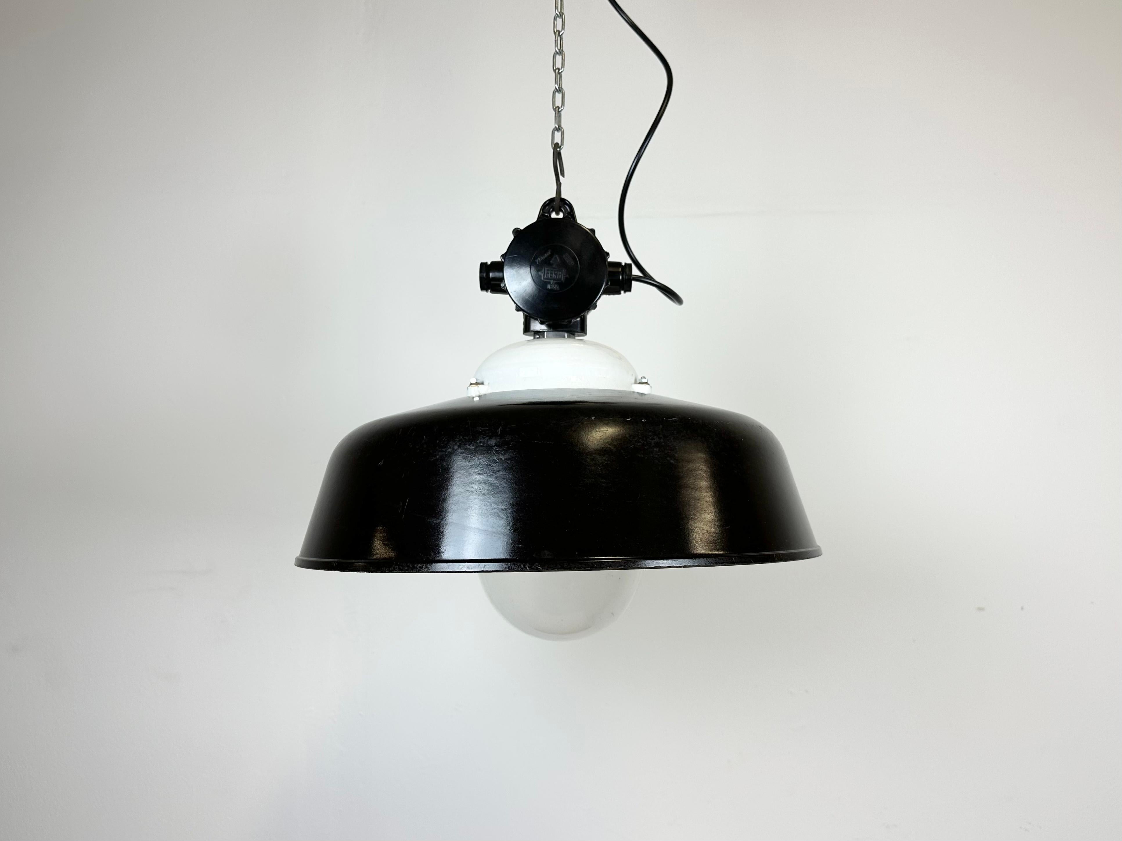 Industrial factory light made in Germany during the 1950s. It features a black enamel shade with white interior, a porcelain top with bakelite box and clear glass cover.The socket requires E 27/ E 26 lightbulbs. New wire.The weight of the lamp is