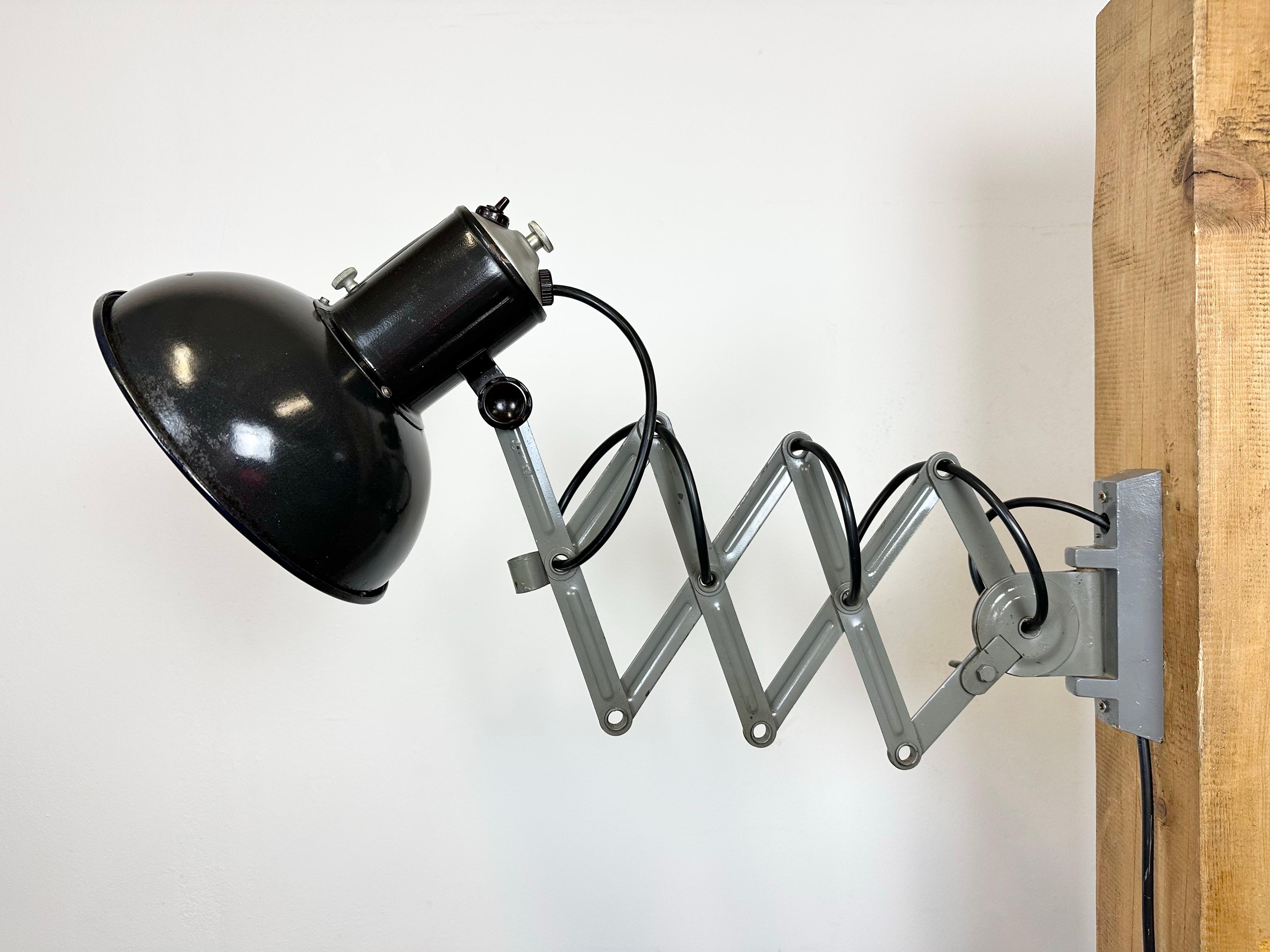 This vintage Industrial scissor lamp was produced in former Czechoslovakia during the 1950s. The lamp has a black enamel metal shade with white enamel interior. Grey iron scissor arm is extendable and can be turned sideways. Porcelain socket