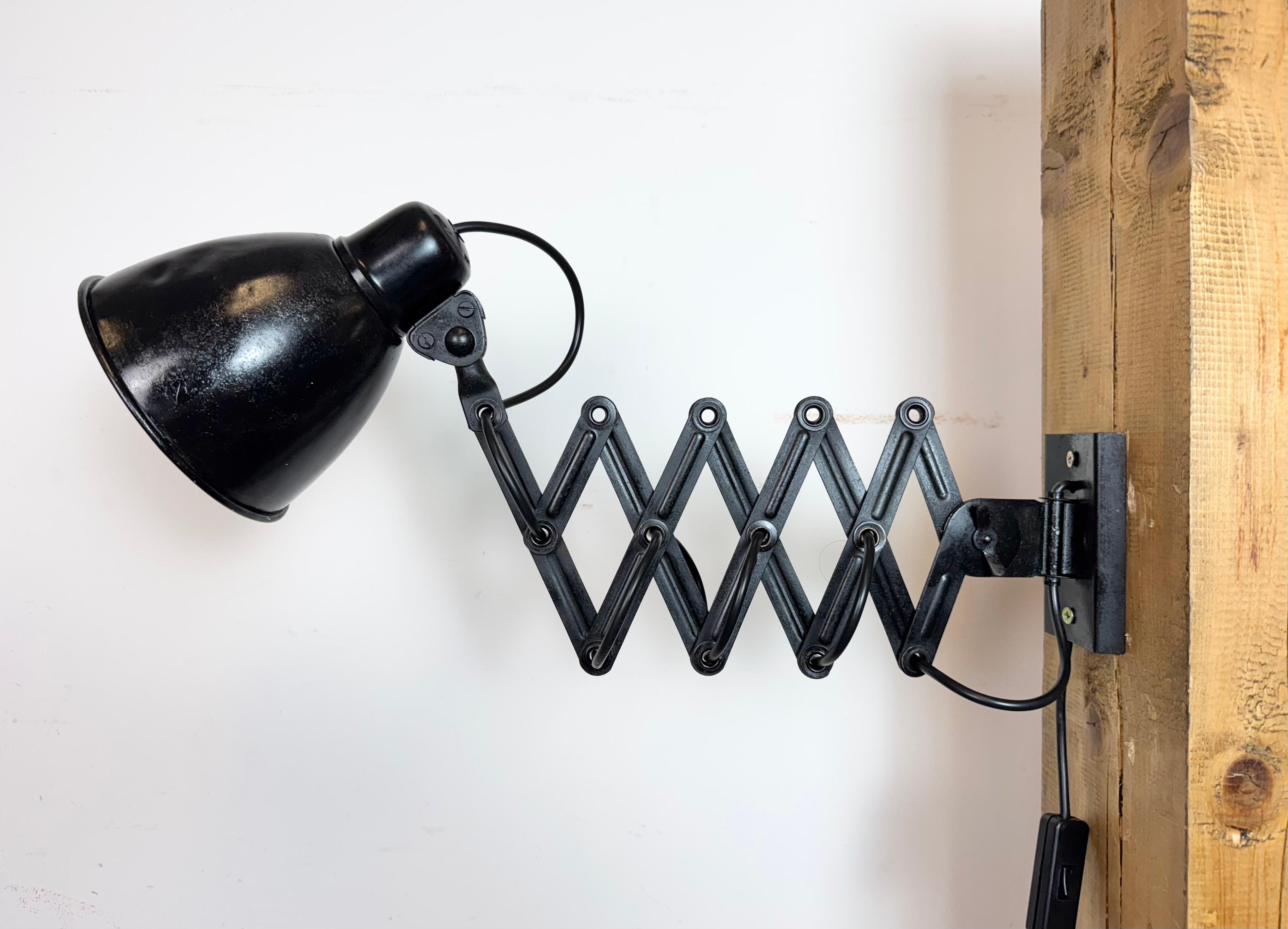 Cette lampe à ciseaux industrielle vintage a été produite dans l'ancienne Tchécoslovaquie au cours des années 1950. La lampe est dotée d'un abat-jour en aluminium noir et d'un couvercle en bakélite. Le bras de ciseaux en fer noir est extensible et