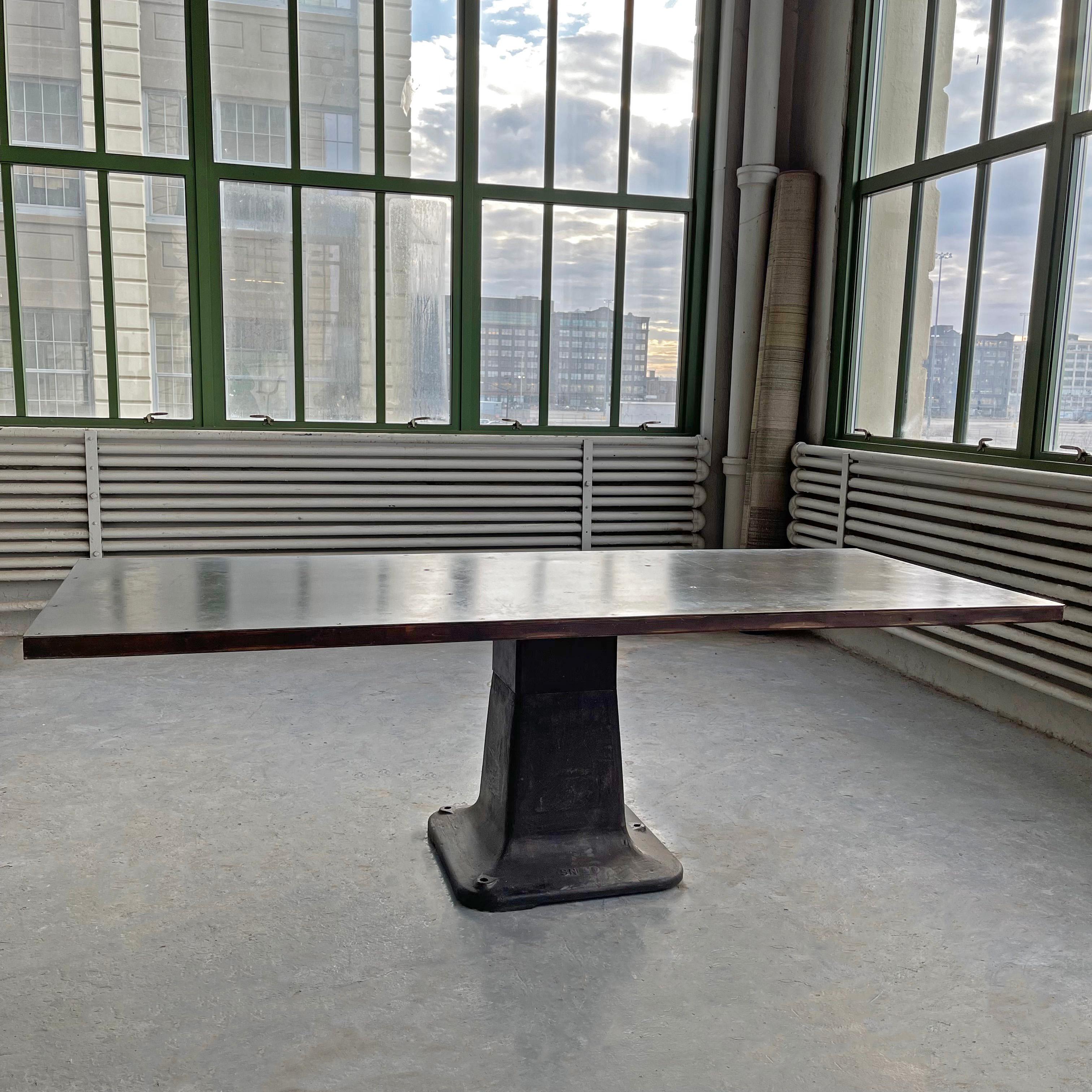 Large, industrial table features a vintage cast iron pedestal base with 21st century fabricated, riveted, blackened steel plate and maple top. The table has a fantastic patina througout and is perfect as a dining, conference or work table.