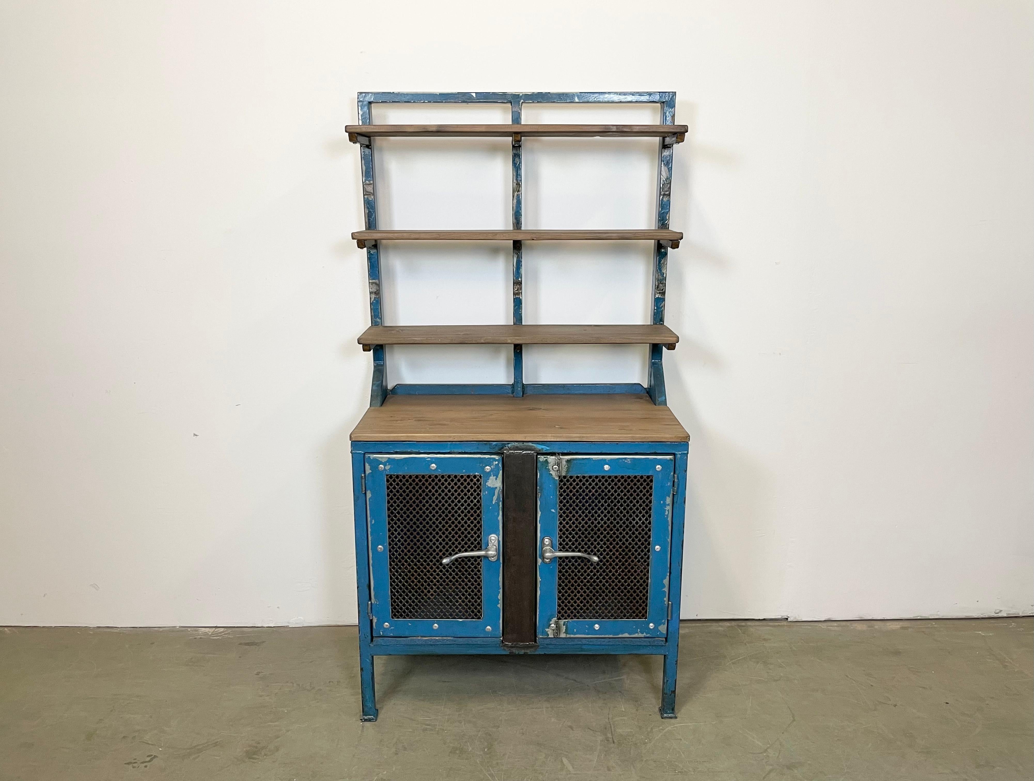 Vintage industrial cabinet made during the 1960s. It features a blue iron construction with mesh doors , wooden top and three wooden shelwes. The weight of the cabinet is 57 kg.