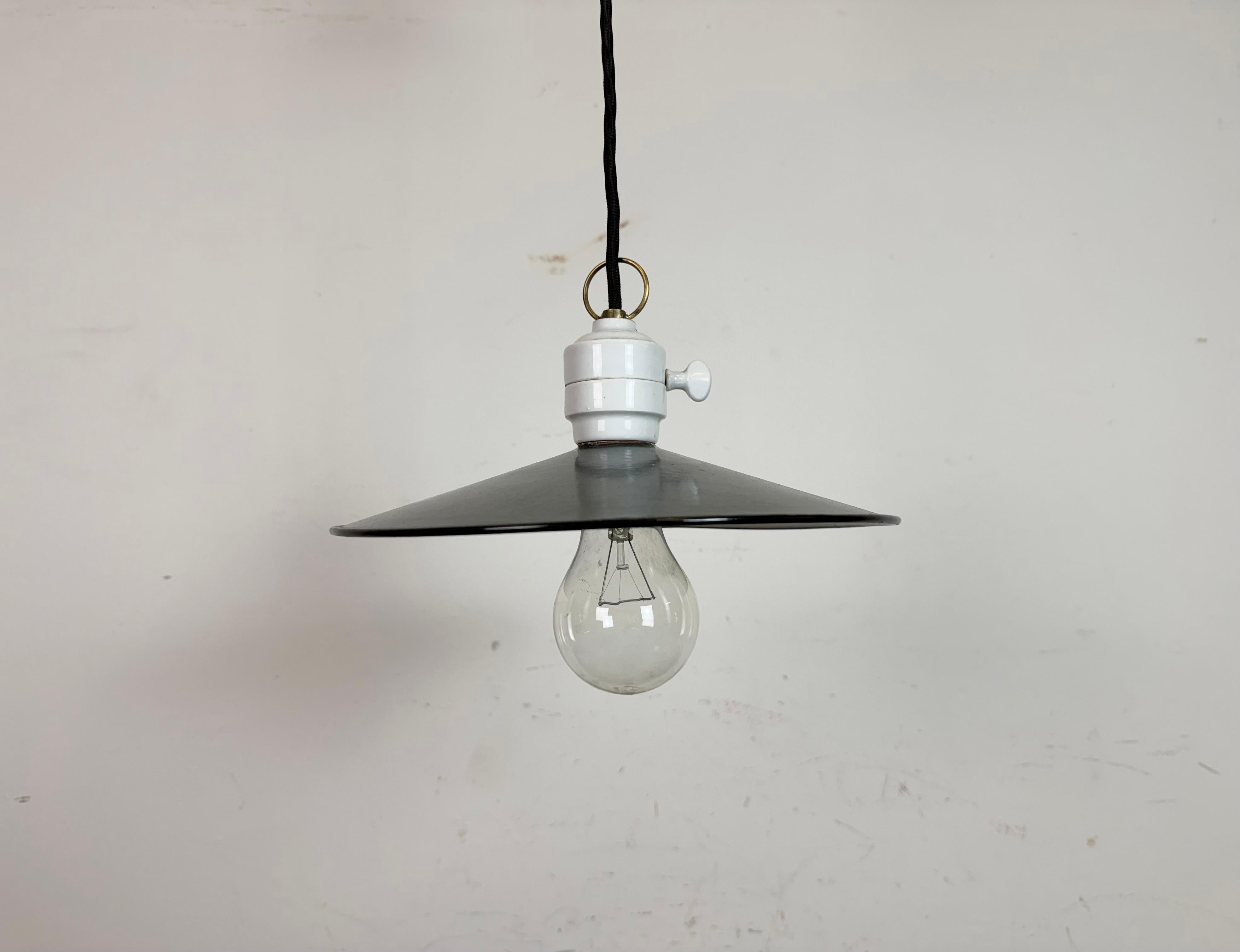Lampada da soffitto industriale smaltata vintage realizzata nell'ex Cecoslovacchia negli anni '50. Presenta un paralume in smalto blu con interno in smalto bianco, un piano in porcellana con interruttore e un rosone in porcellana. L'attacco richiede