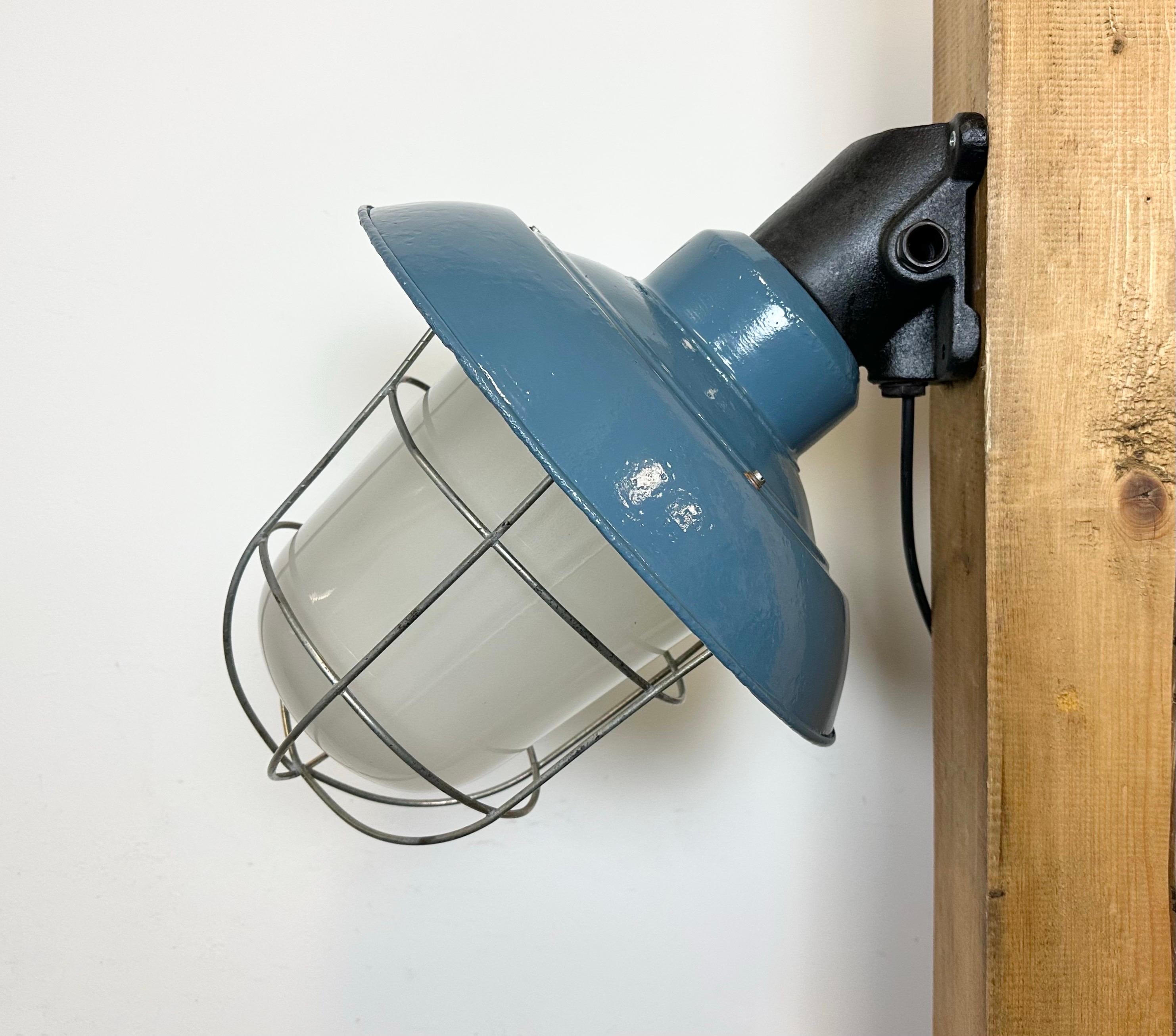 This Industrial wall lamp was designed in the 1960s and produced by Elektrosvit in the former Czechoslovakia. It features a black cast iron wall mounting, a newly blue painted shade with a white enamel interior, a milk glass cover and an iron grid.