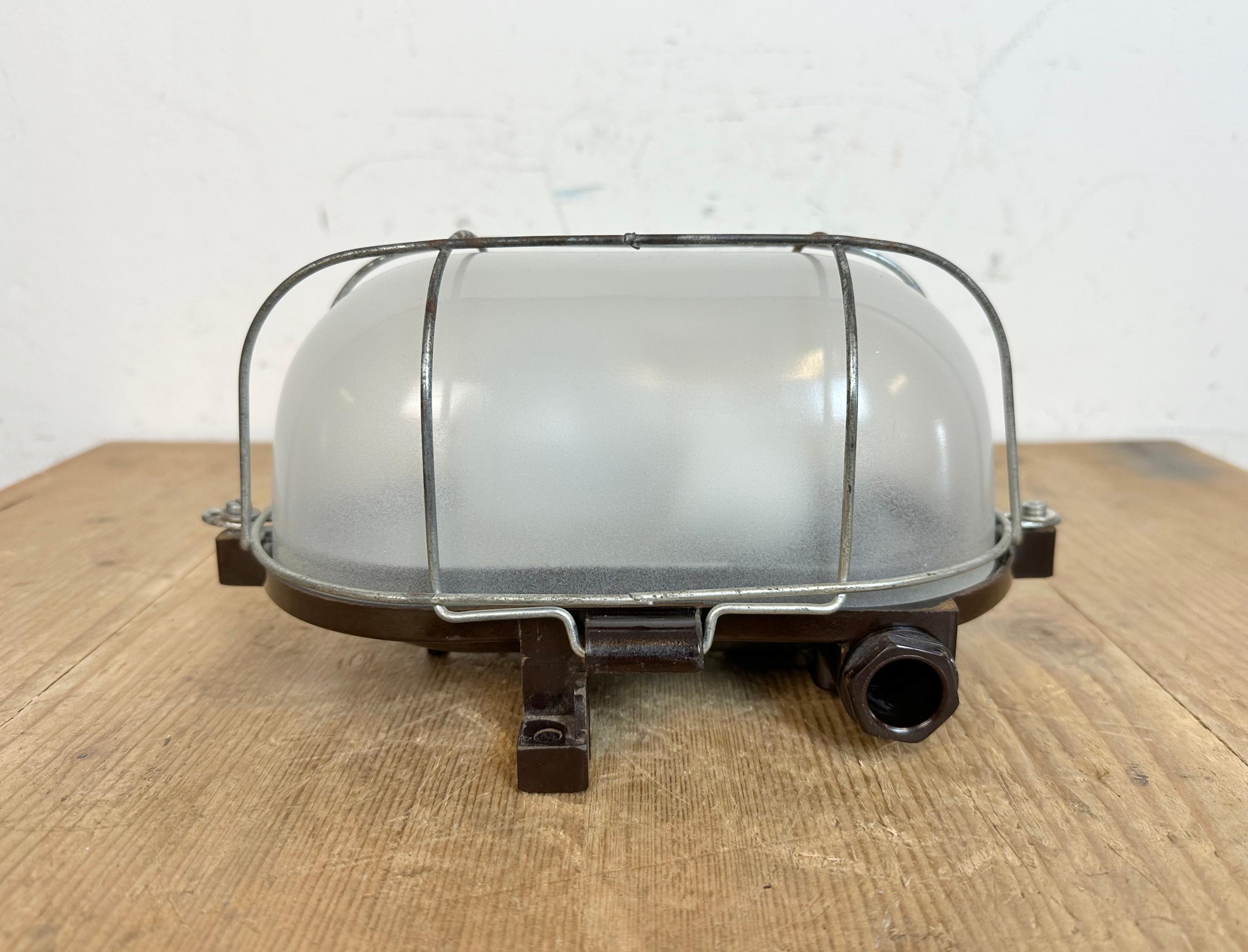 Vintage industrial brown bakelite wall lamp made in former Czechoslovakia during the 1960s. It features a bakelite body, a milk glass cover and iron grid.The socket requires standard E 27/E 26 light bulbs.  Weight of the lamp is 1 kg.