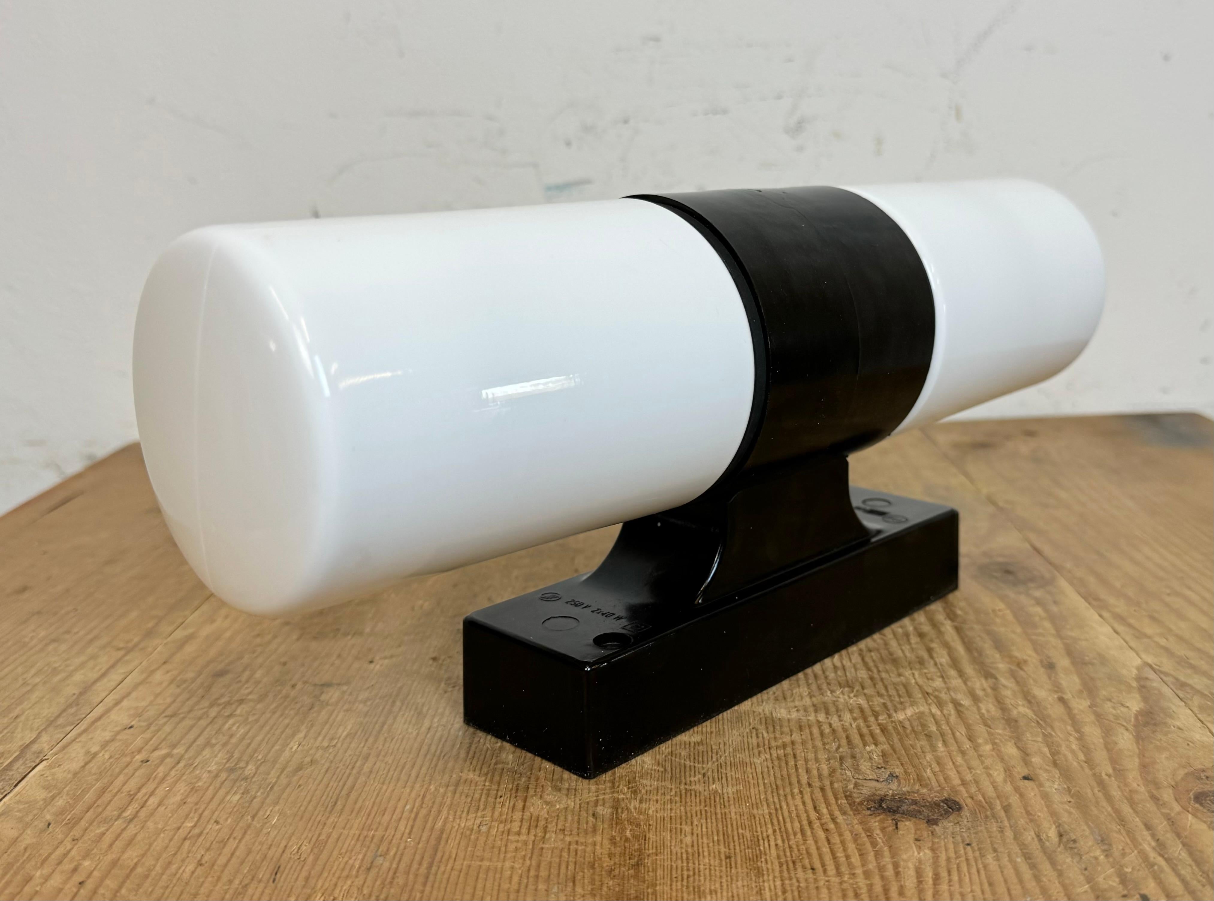 Vintage industrial brown bakelite wall lamp made in former Czechoslovakia during the 1960s. It features a bakelite wall mounting and two milk glass covers. The sockets require two E 14 light bulbs.  Weight of the light is 0,9 kg.