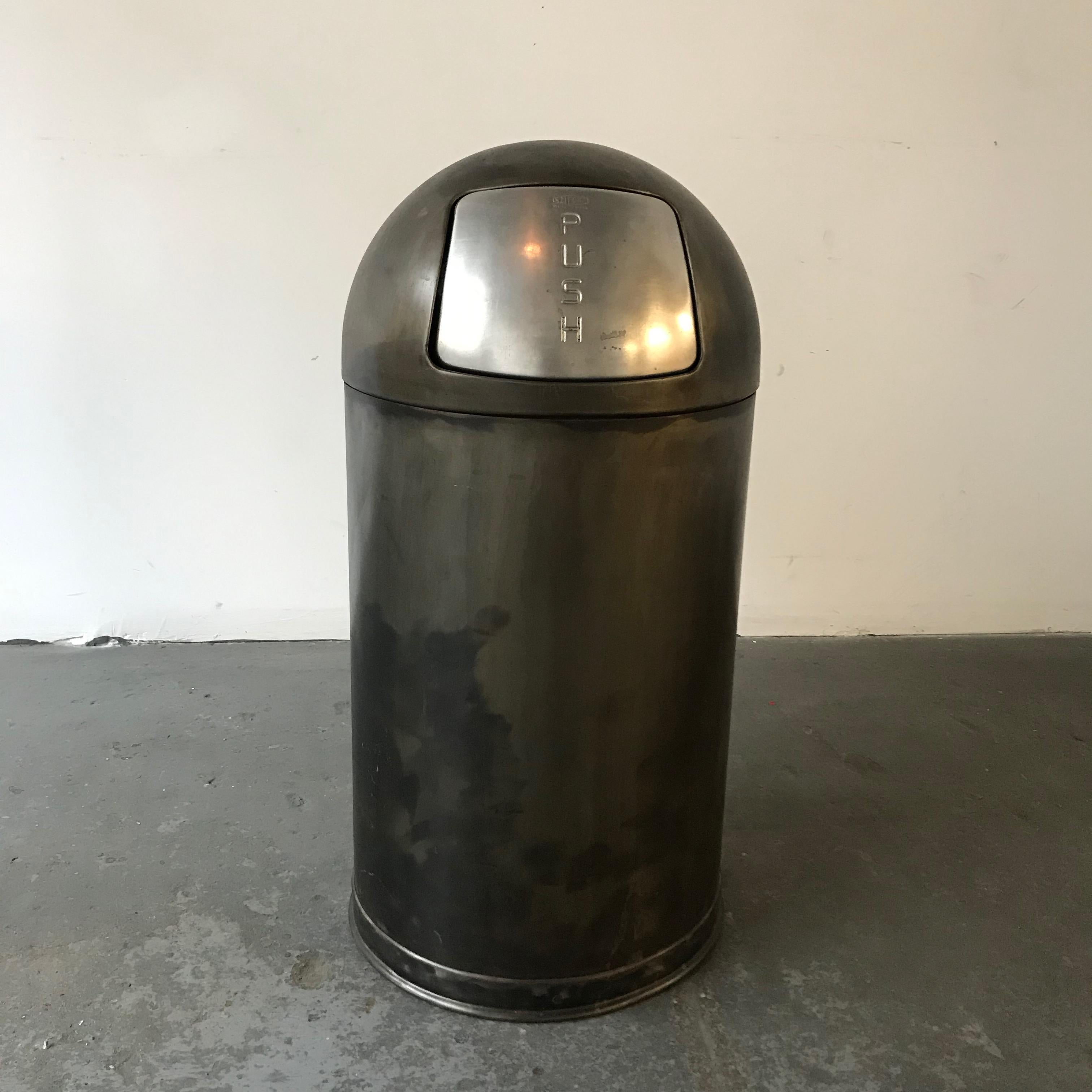 Industrial, midcentury, trash can features a gunmetal steel finish, bullet shaped exterior with push top that fits over a galvanized steel trash receptacle.