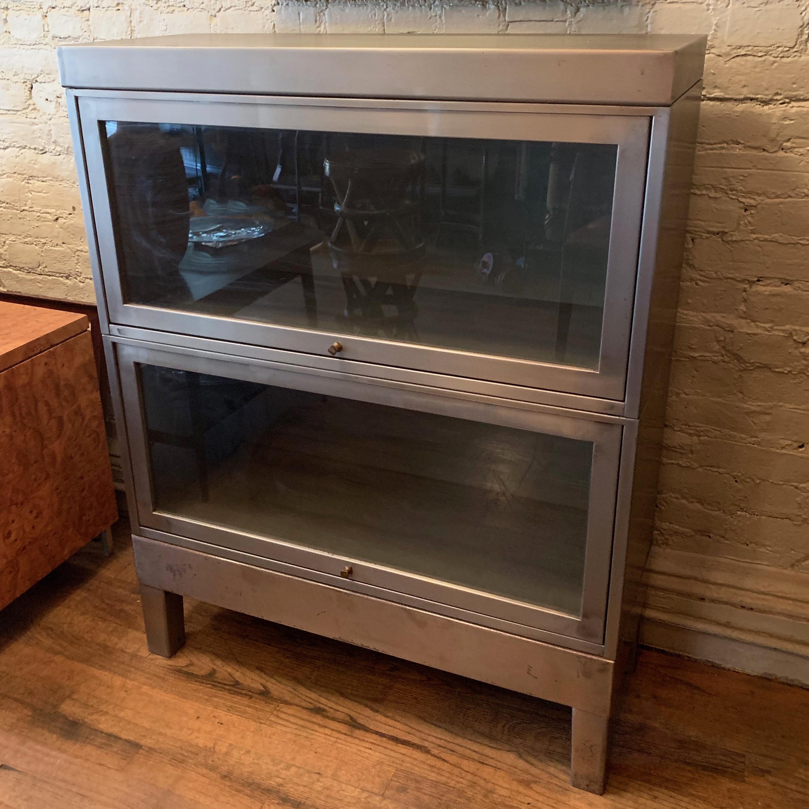 Industrial, brushed steel, barrister book case or cabinet by Globe Wernicke features two, interlocking, stackable cases with glass front doors that slide to open with brass pulls and painted gray interiors. The interior height of the cases measures