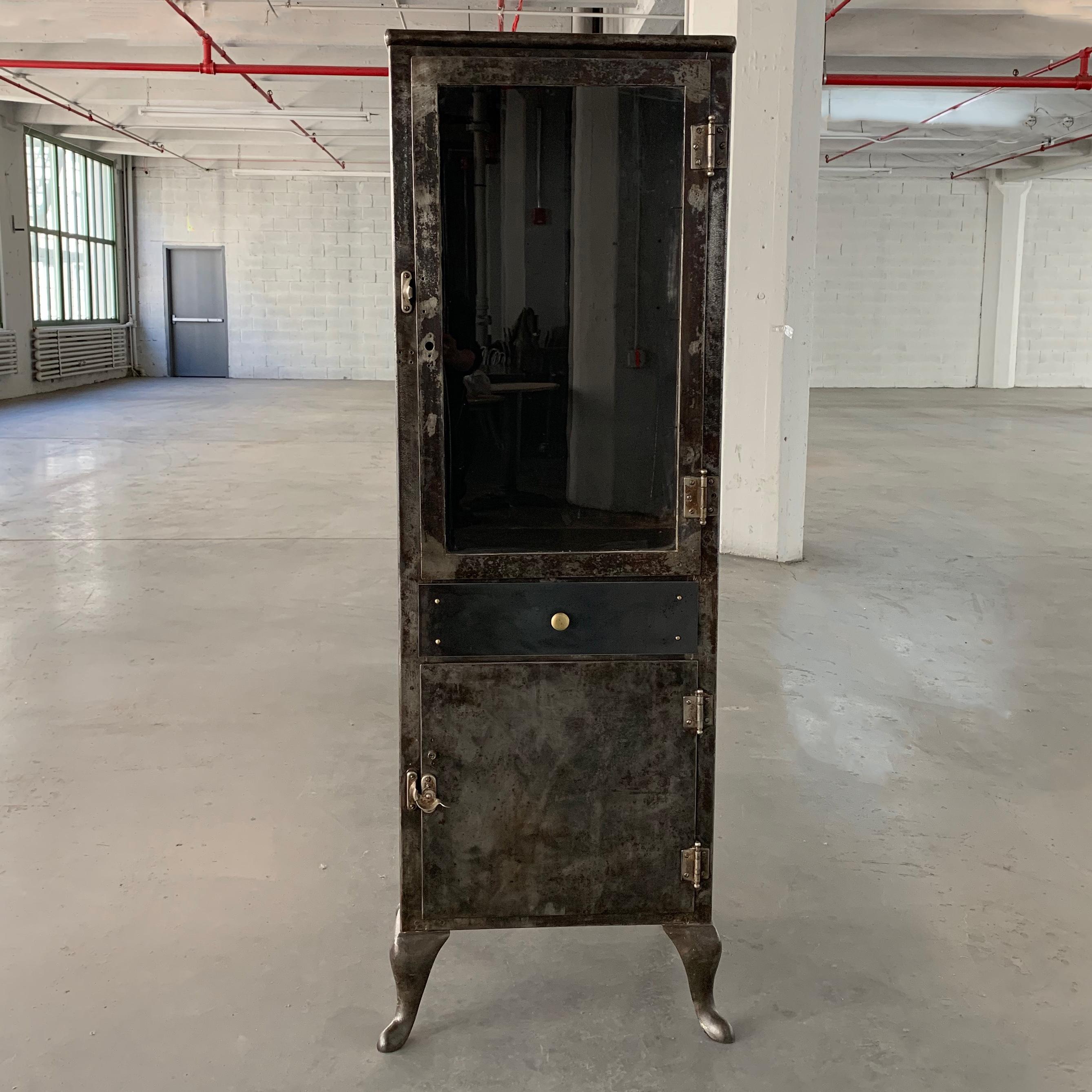 Early 20th century, industrial, brushed steel, apothecary cabinet features glass front, display on top that measures 31.5 inches height inside and closed storage below. 2 glass shelves are included for the top interior.