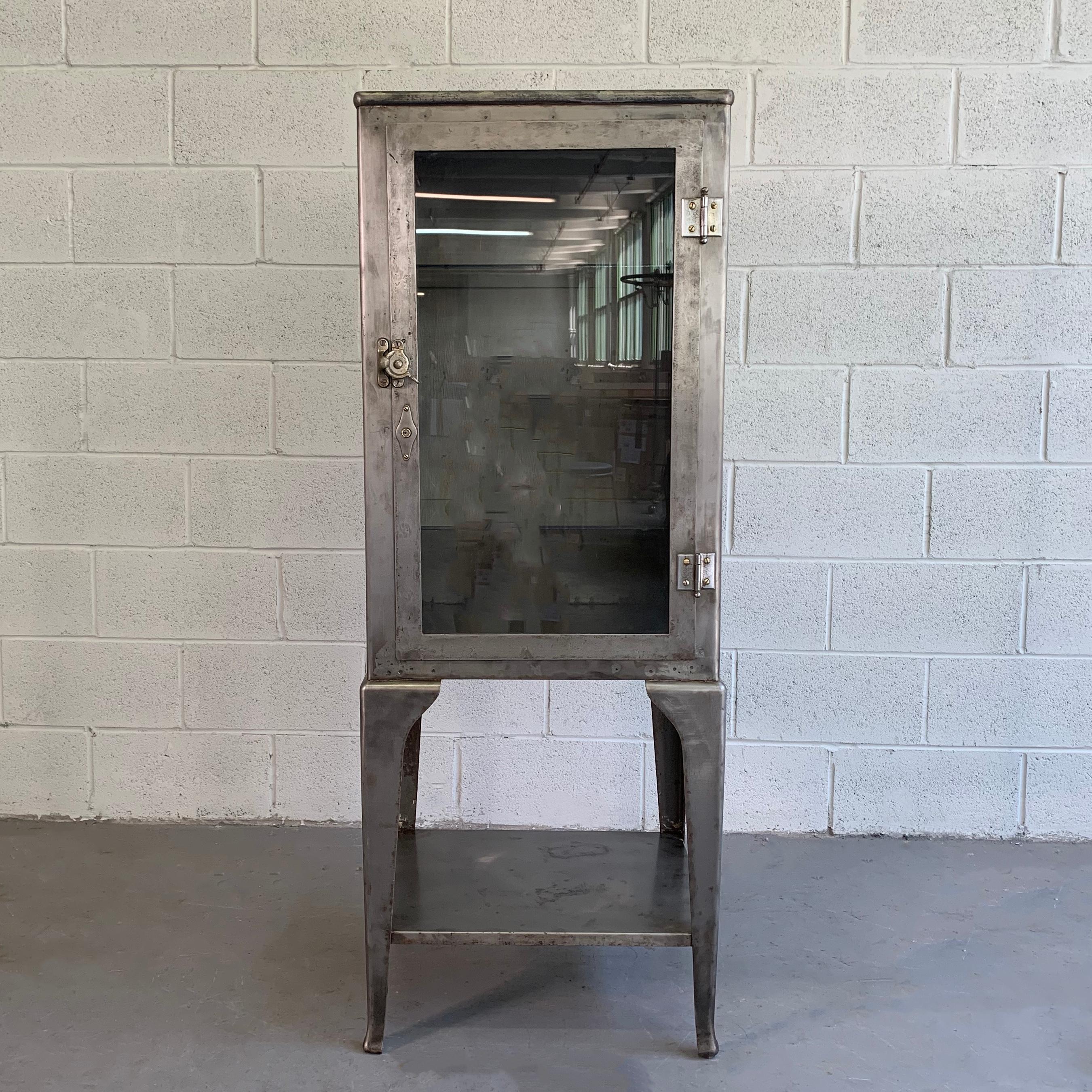 Early 20th century, industrial, brushed steel, apothecary, display cabinet features a latched glass front with two interior glass shelves and an open shelf on the bottom. The cabinet is newly brushed inside and out.
