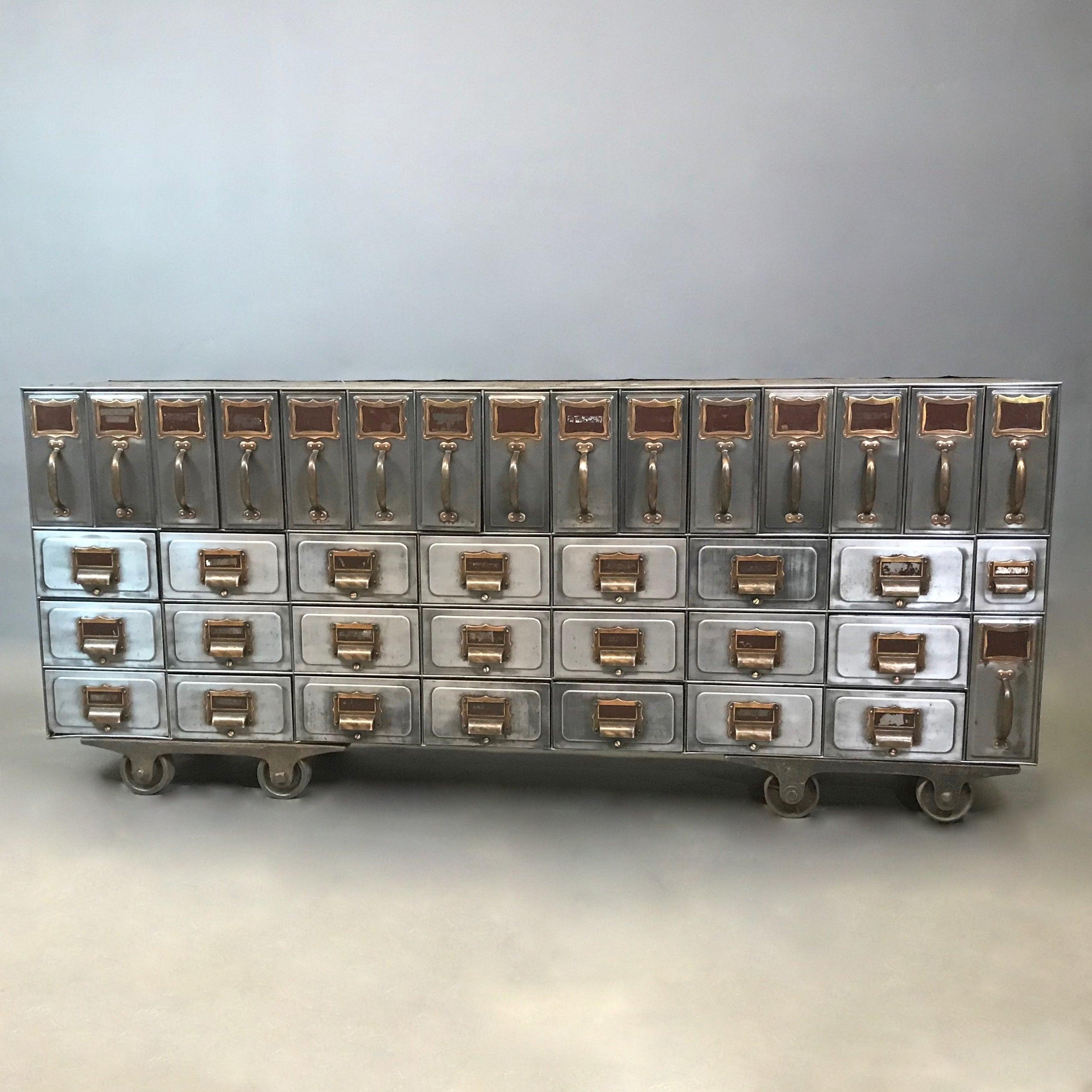 Rare, early 20th century, industrial, brushed steel, file storage console features 38 drawers in a unique linear configuration with brass cup pulls, handles and name plates on cast iron, rolling dollies. The console has an unfinished top that can