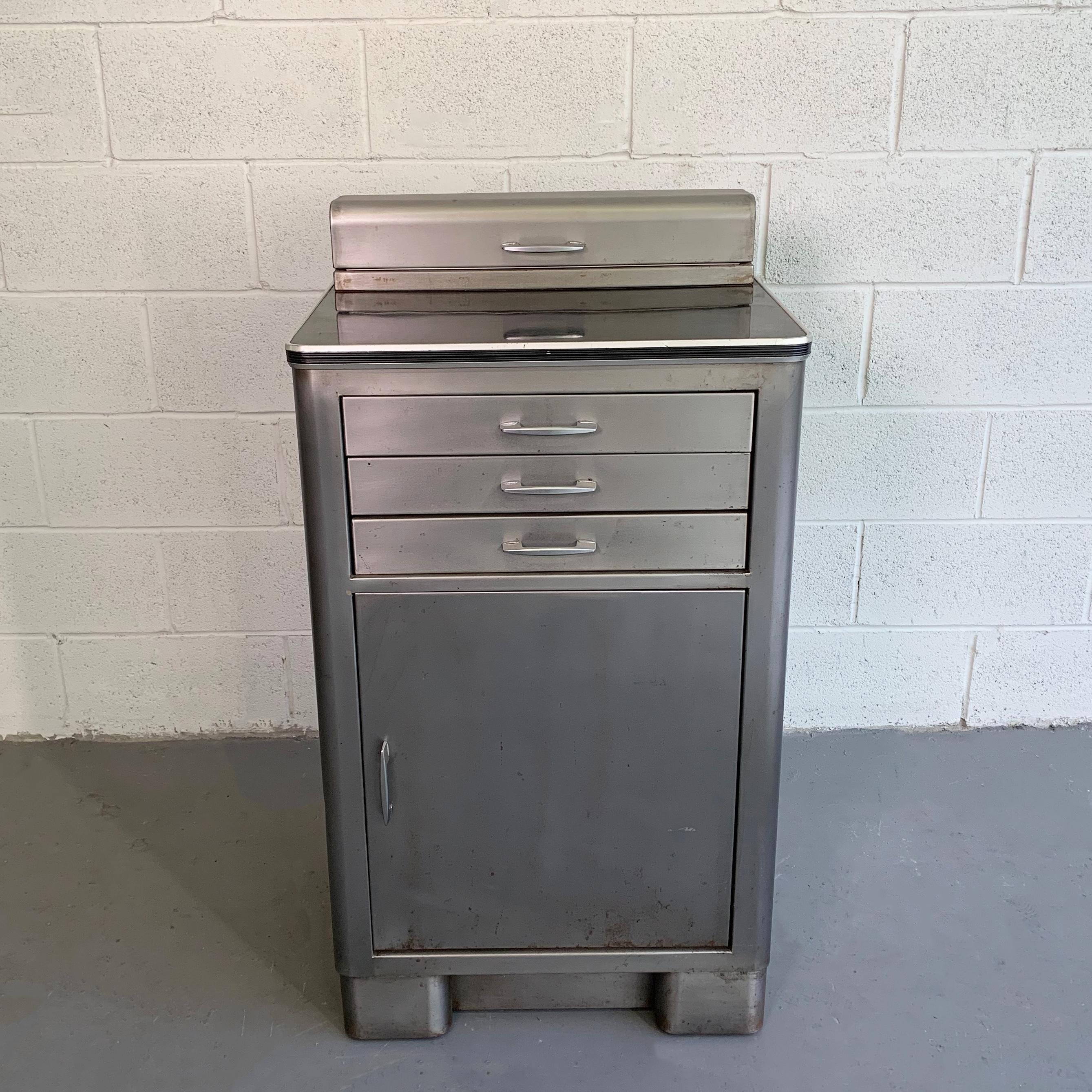 Industrial, brushed steel, nurse station, medicine cabinet features a black formica top with bottom cabinet at 20 inches height and 15 inches deep and three 1.5 inch height drawers with original green interiors and medicine storage on top.