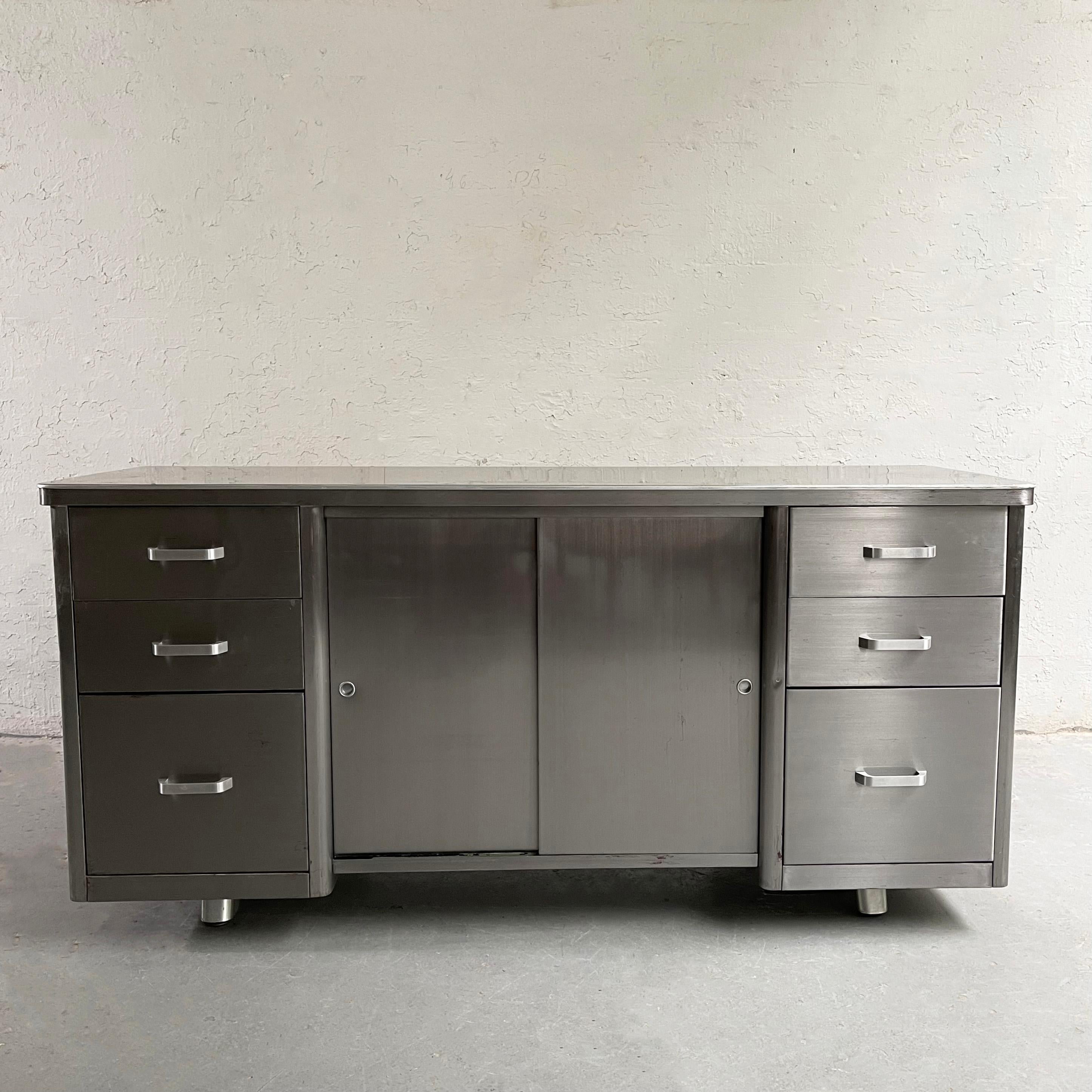 Midcentury, industrial, brushed steel, office credenza cabinet features drawers on both sides with sliding door shelf storage in the middle. The bottom drawers can hold file folders with an added frame. The cabinet is an interesting credenza