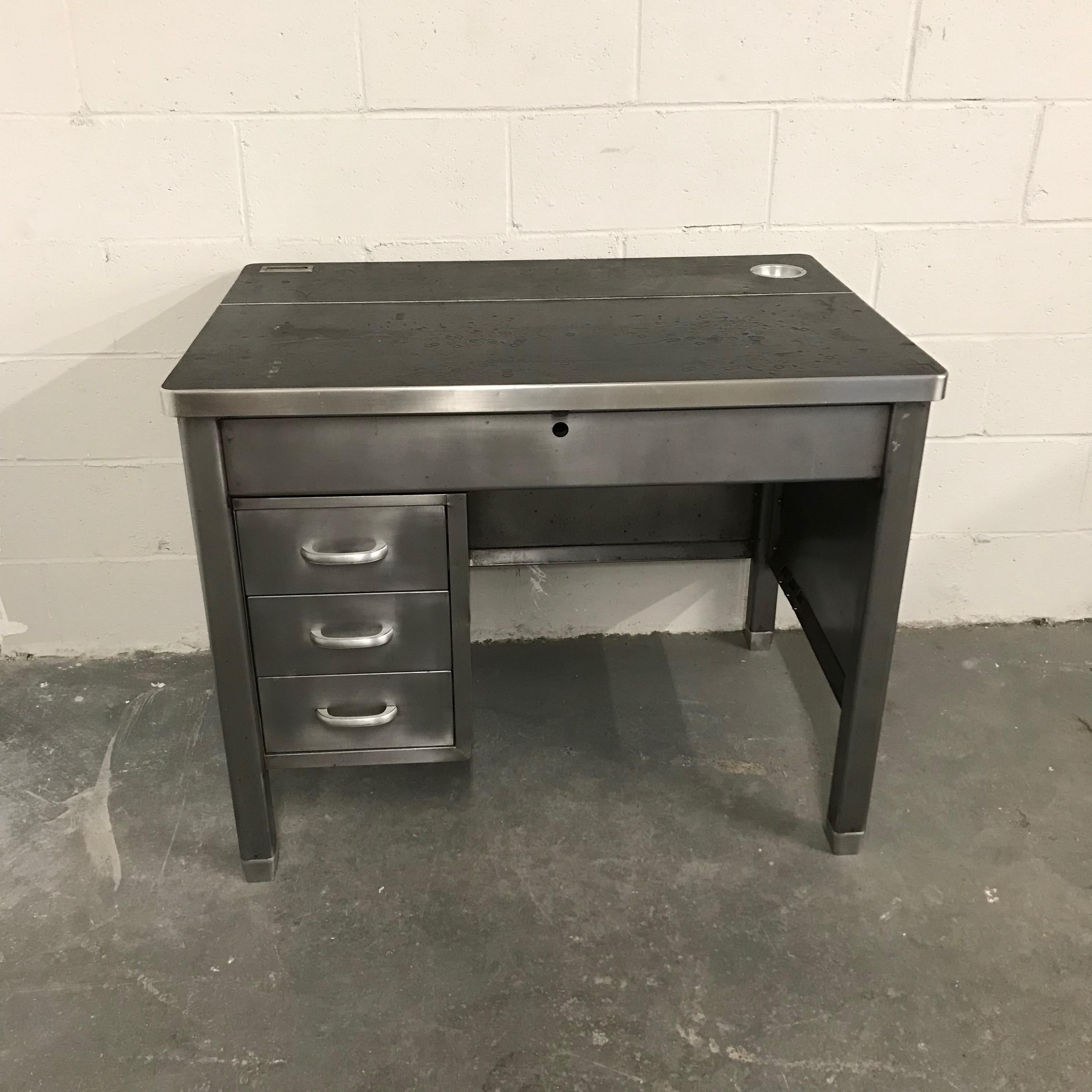 Industrial, midcentury, military, office desk features a newly brushed steel finish with original rubber top that opens to reveal additional, 4.5 inches deep, security storage underneath. The top includes a recessed paperclip cup at the back and