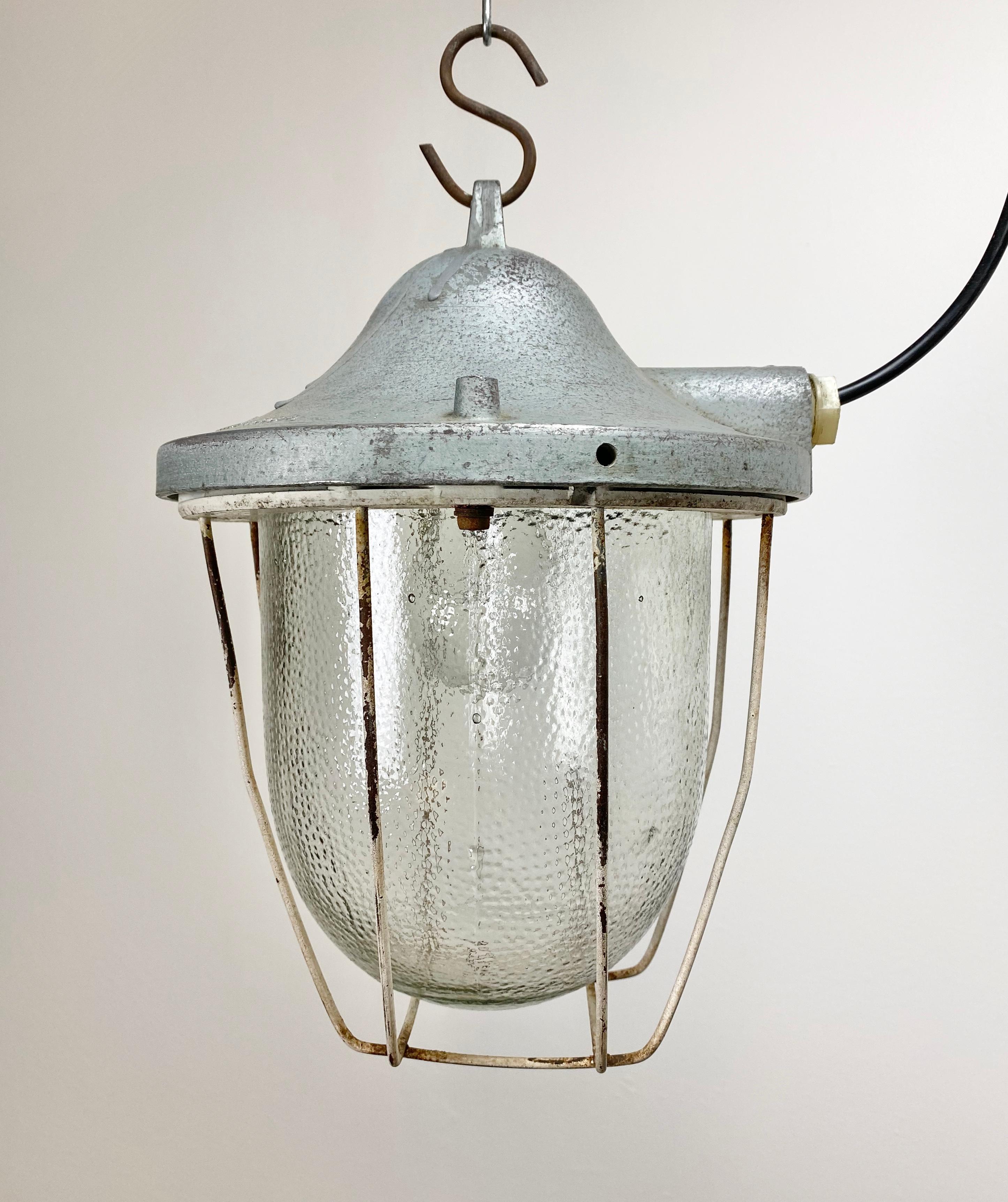 Grey industrial lamp made by Polam Gdansk in Poland during the 1960s. It features a cast aluminium body, an iron cage and frosted glass. The porcelain socket for E 27 lightbulbs and new wire.
 