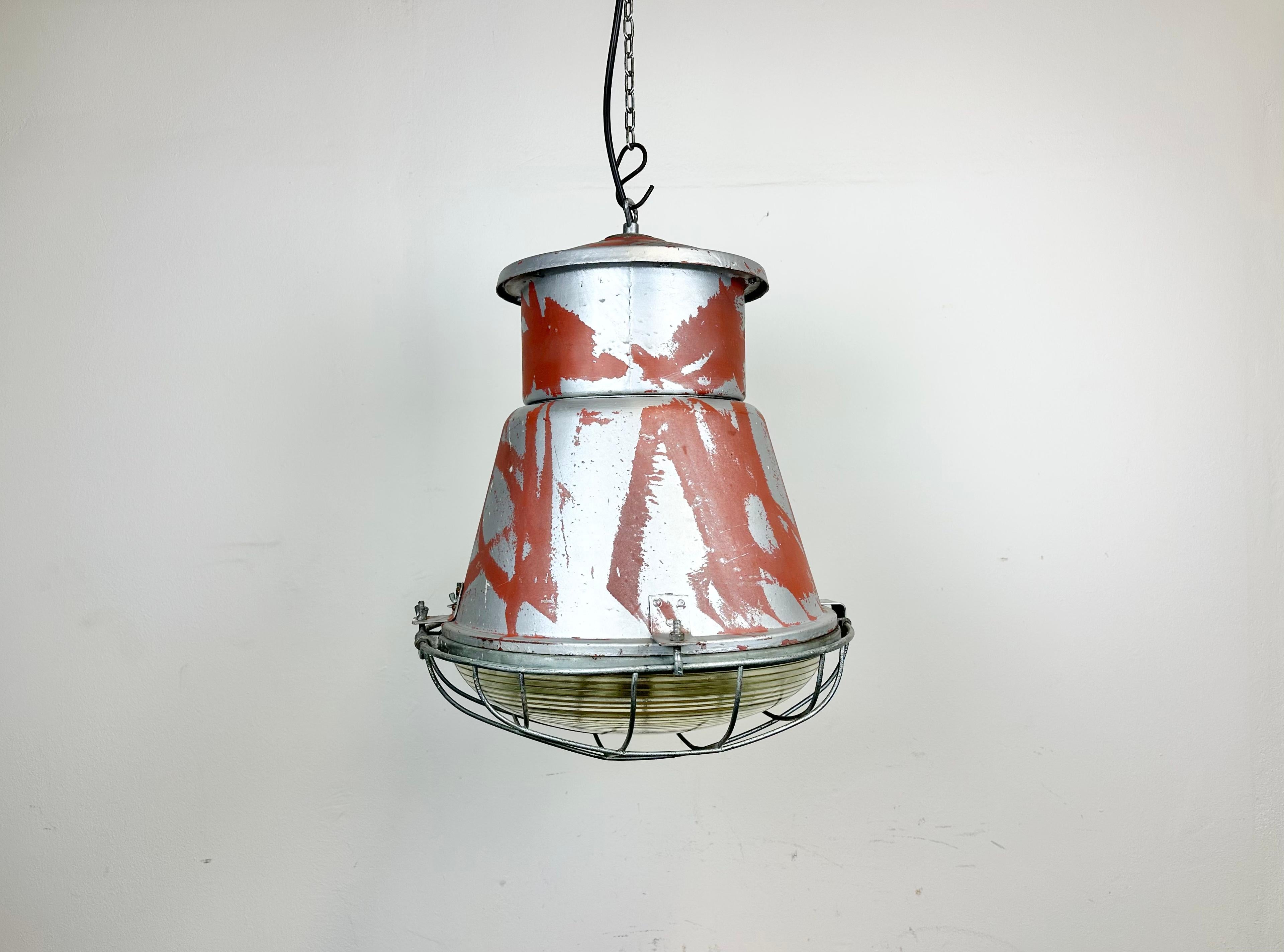 Vintage industrial hanging lamp manufactured in 1970s by MESKO in Skarzysko-Kamienna in Poland. It features a grey iron body, an iron cage and convex glass cover.. The porcelain socket requires E 27/ E26 light bulbs. New wire. The weight of the lamp