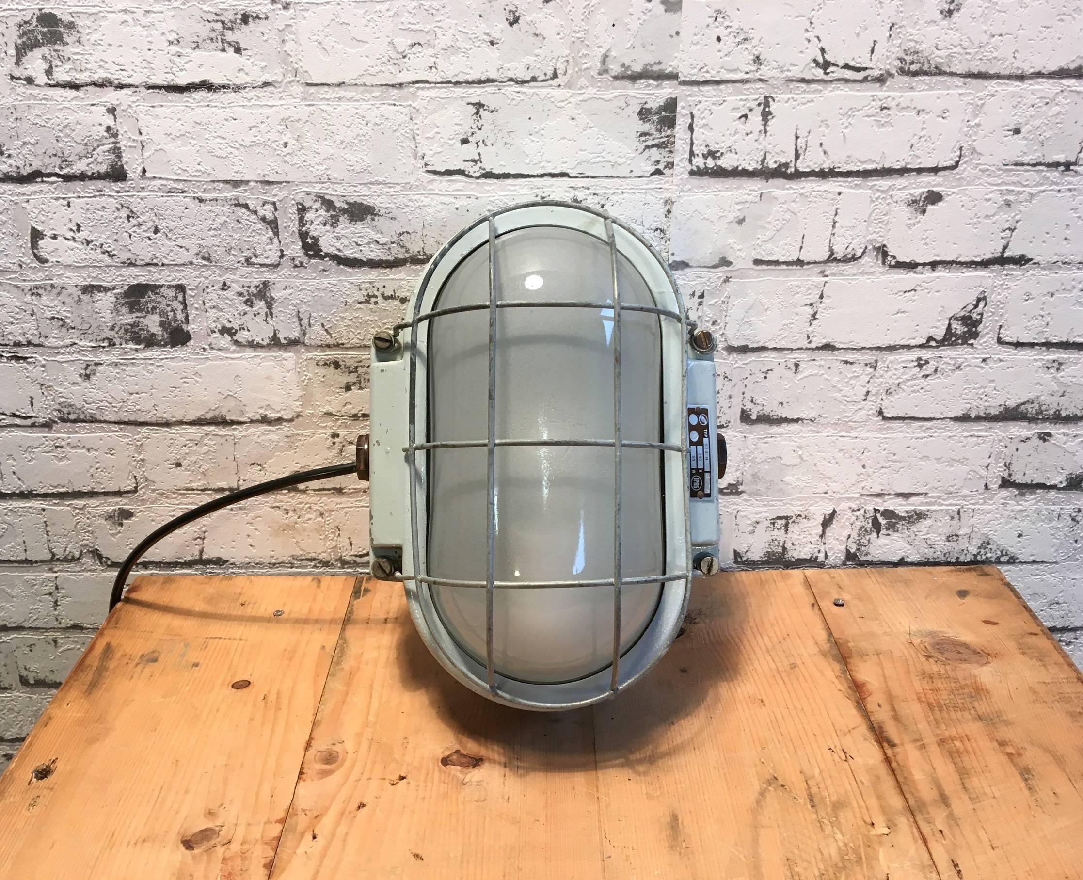 This cast aluminium wall lamp originates from former Czechoslovakia i. It has new porcelain E27 socket, a frosted glass and steel grid. Weight: 3 kg.