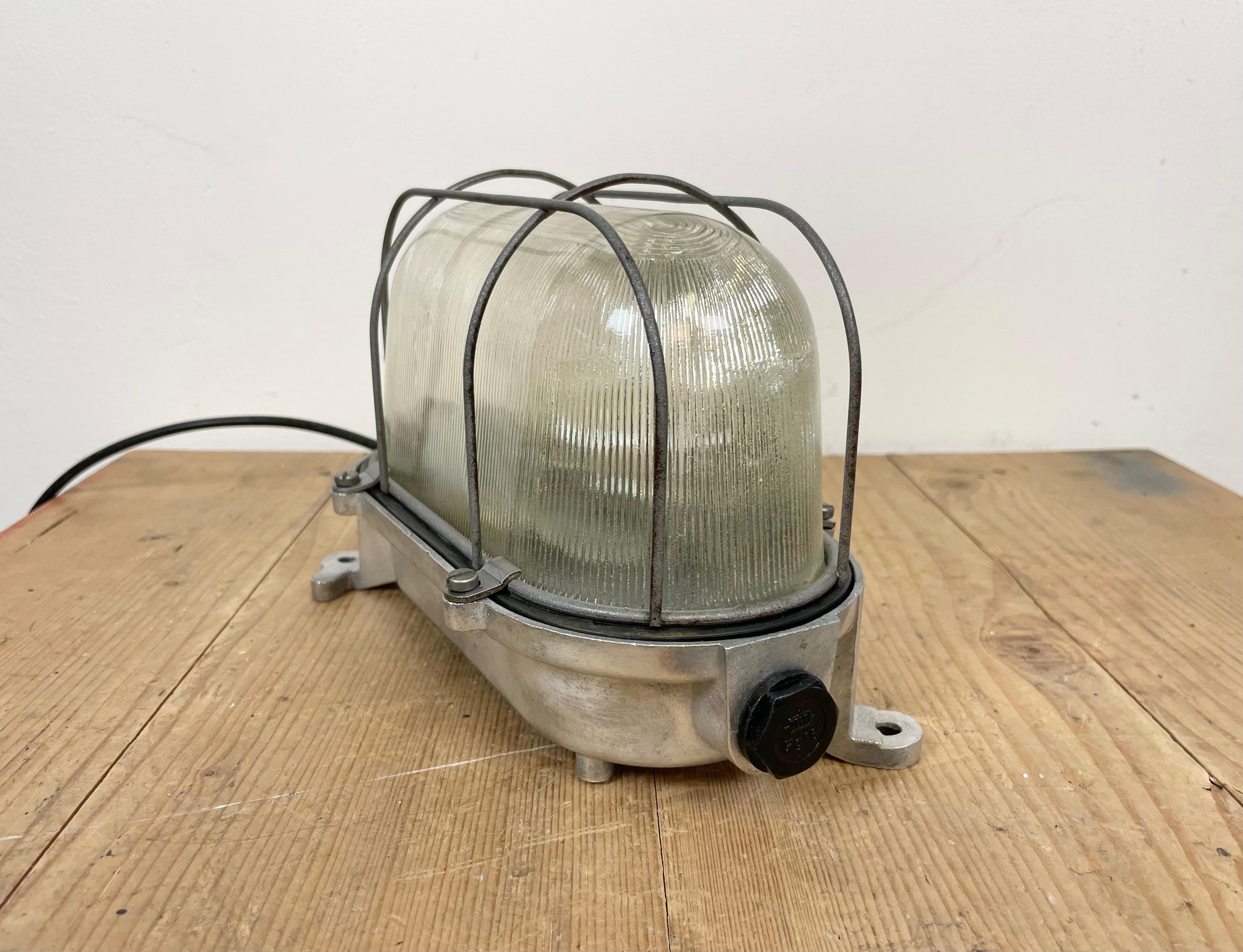 Industrial wall light made in Germany during the 1970s. It features a cast aluminium body, a stripped glass and a steel grid.The porcelain socket requires E 27/E 26 light bulbs. New wire. The weight of the lamp is 1,7 kg.