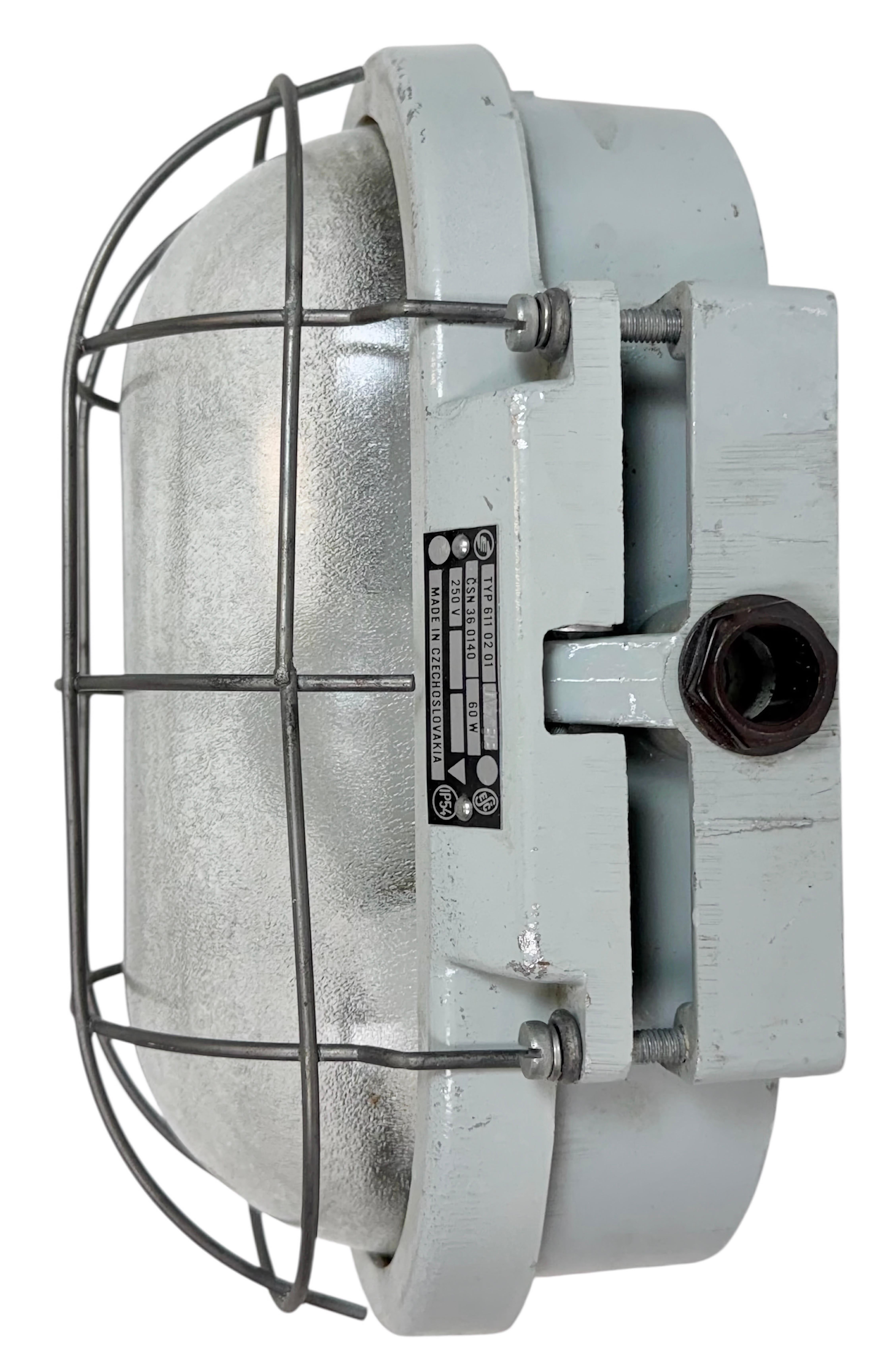 Cette applique industrielle a été fabriquée par Elektrosvit dans l'ancienne Tchécoslovaquie au cours des années 1970. Il est doté d'un corps en fonte d'aluminium, d'un couvercle en verre dépoli et d'une grille en acier. La douille en porcelaine est