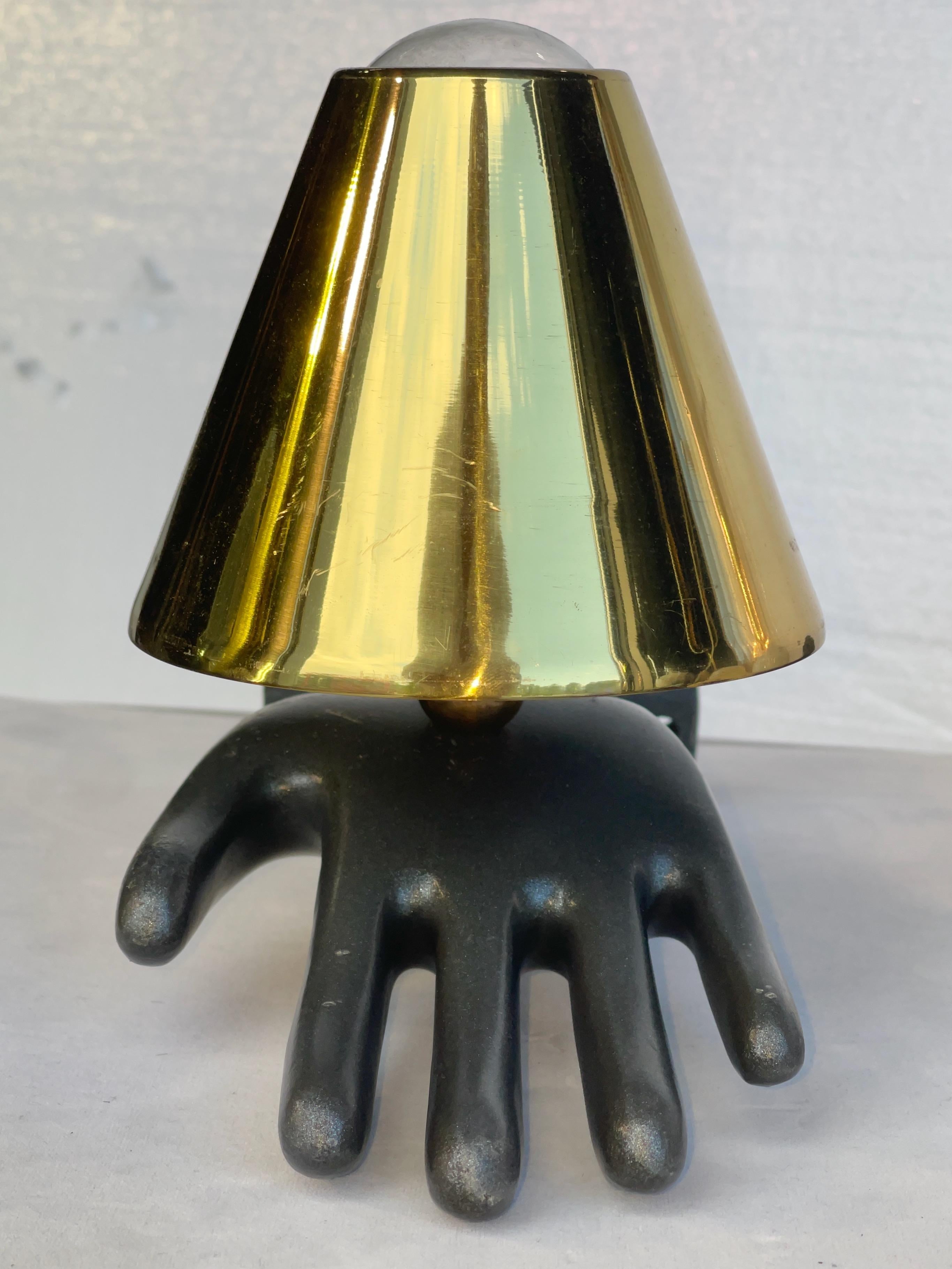 Stampo per guanti da fabbrica in metallo fuso dell'inizio del XX secolo adattato a lampada da parete con presa per lampadina nel palmo della mano aperta. 
Il metallo è di colore grafite e sembra essere fatto di alluminio fuso o di un'altra