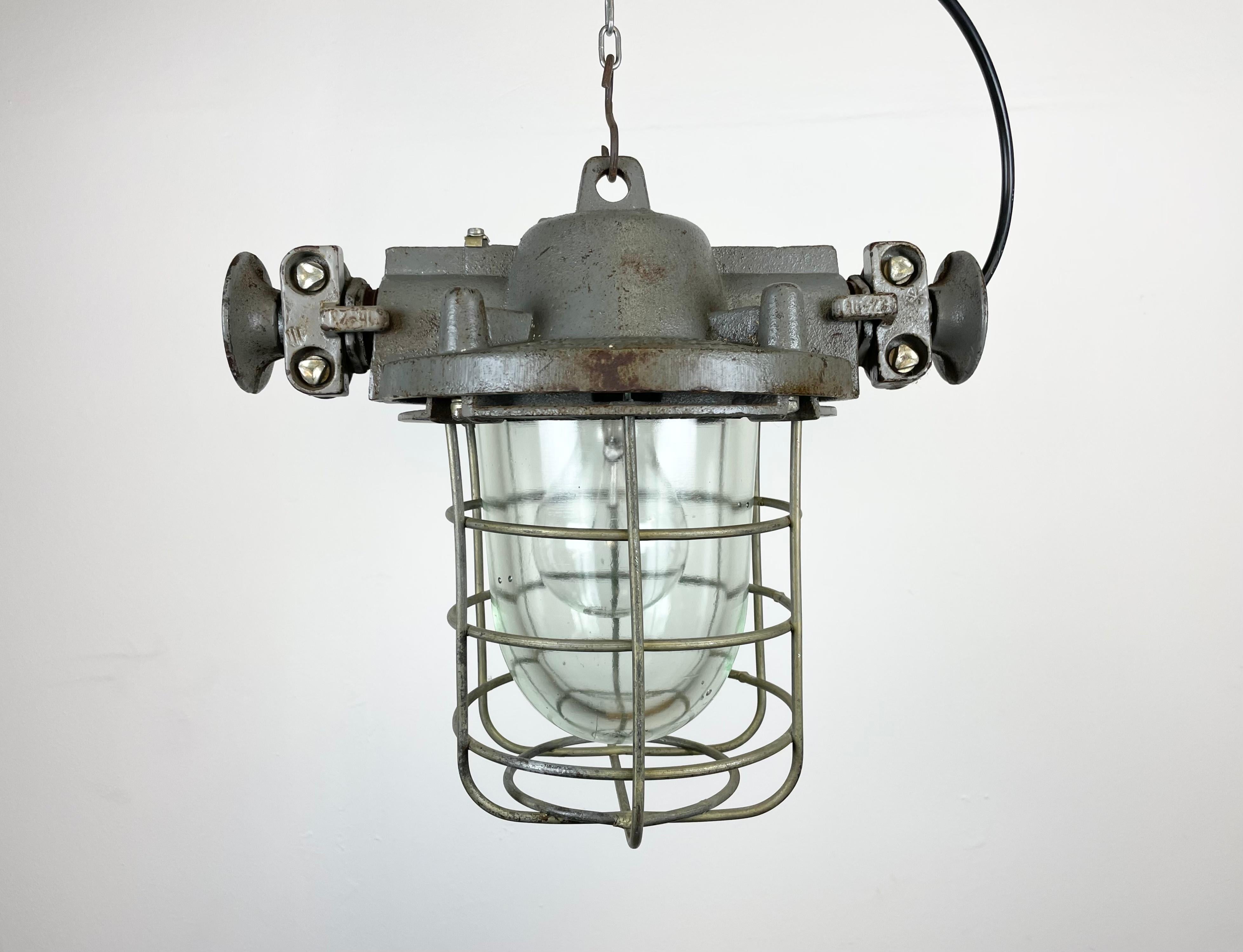 Industrial exposion-proof hanging lamp made in Poland during the 1960s. These lamps were used in factories where was a danger of gas or dust explosion. It features a cast iron body, a clear glass cover an an iron grid. The porcelain socket requires