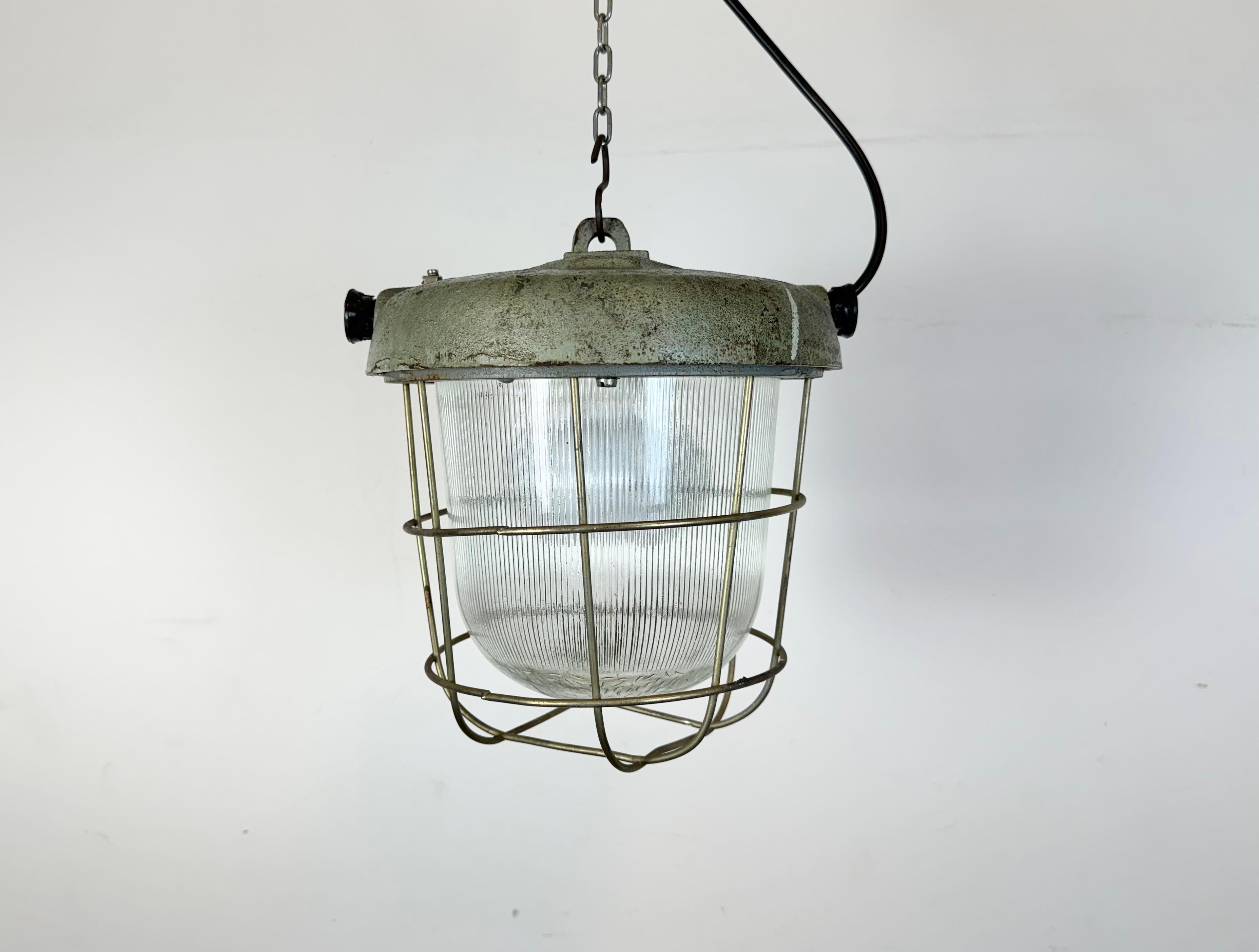 Industrial factory hanging lamp made by Polam Wilkasy in Poland during the 1960s.It features a cast iron top, a striped glass cover and an iron grid. The porcelain socket requires standard E27 / E26 lightbulbs. New wire. The weight of the lamp is