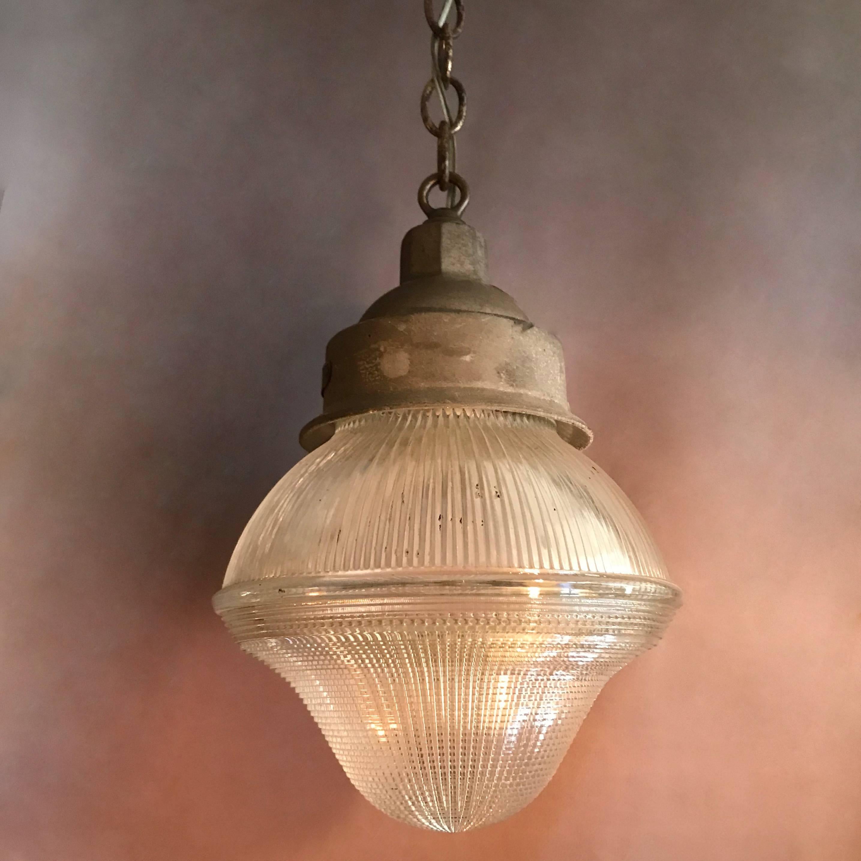 Industrial, factory, pendant light features an acorn shape, Holophane glass shade with contrasting prismatic patterns on a cast iron fitter and steel chain and canopy that hangs 30 inches fully extended. The pendant is newly wired to accept up to a