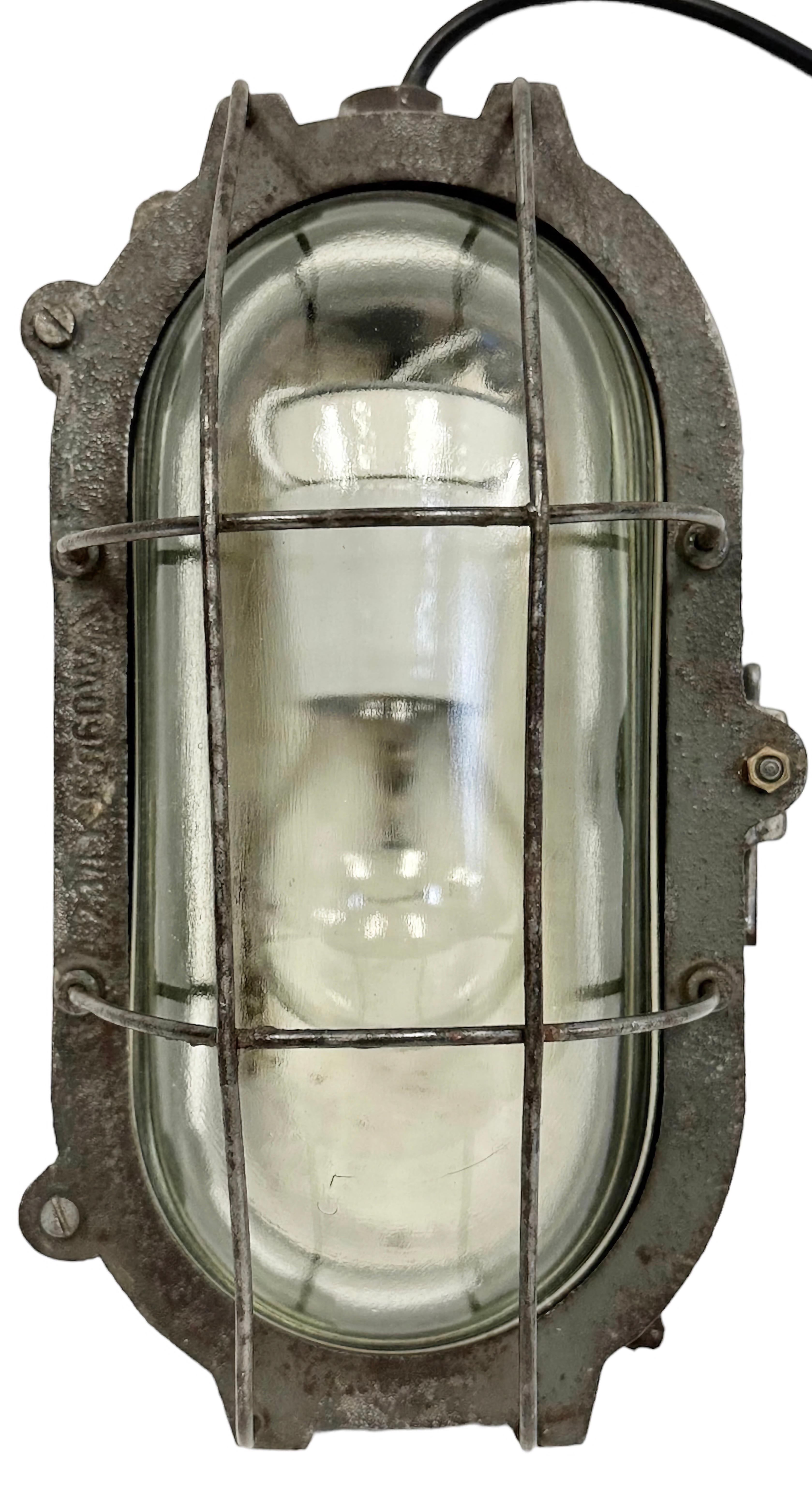 Industrial wall light made in Poland during the 1960s. It features a cast iron body, a clear glass cover and a steel grid.The porcelain socket requires E 27/ E 26 light bulbs. New wire. The weight of the light is 3.7 kg.