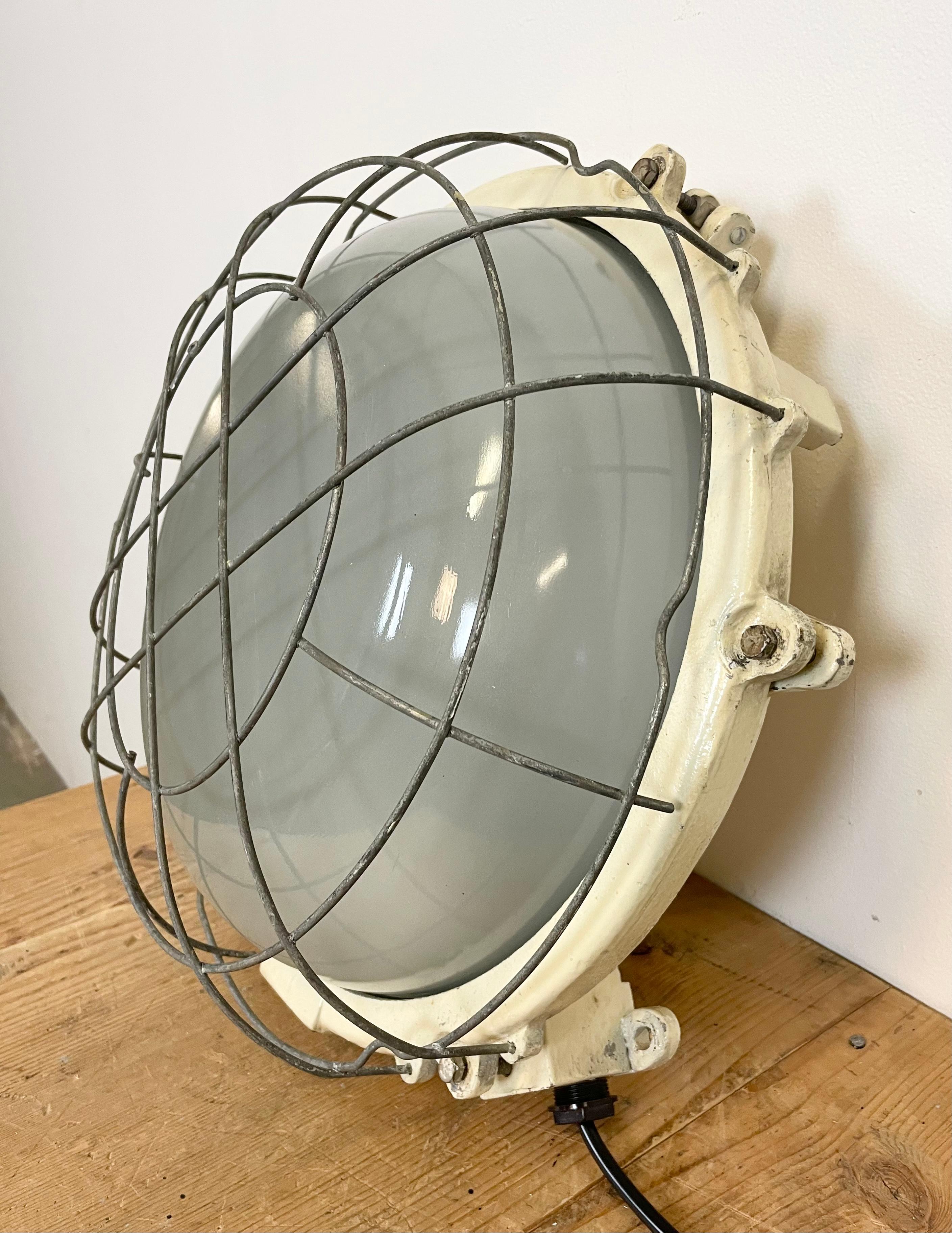 Vintage industrial cast iron wall lamp made by Elektrosvit in former Czechoslovakia during the 1970s. It features a cast iron body, milky curved glass cover and iron grid. Two porcelain sockets require E 27 light bulbs. It can be also used as a