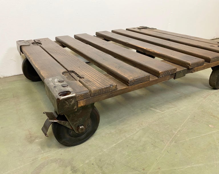 Former pallet truck from a factory now serves as a coffee table. It features four original wheels mounted on a solid wooden top. The weight of the table is 14 kg.