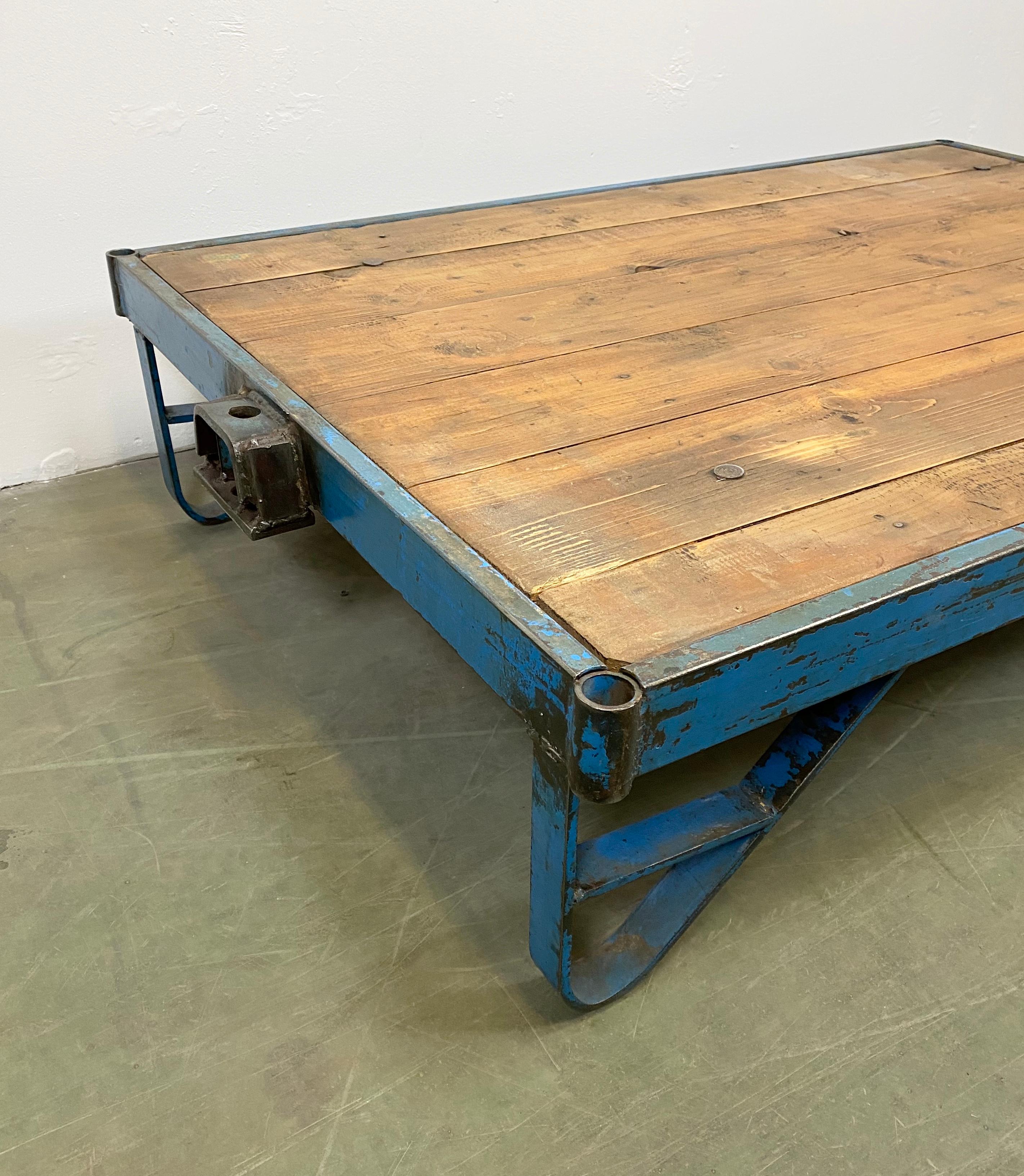 Former pallet truck from a factory now serves as a coffee table. It features a blue iron construction with two wheels and a solid wooden plate. The weight of the table is 40 kg.