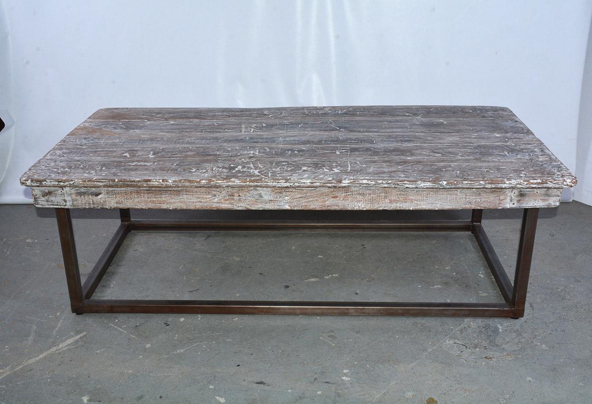 The industrial coffee table is composed of an antique table top and apron with rubbed white paint and a contemporary base of iron tubing. The corners of the apron are secured with tin plates that have been nailed to it. This could be the main