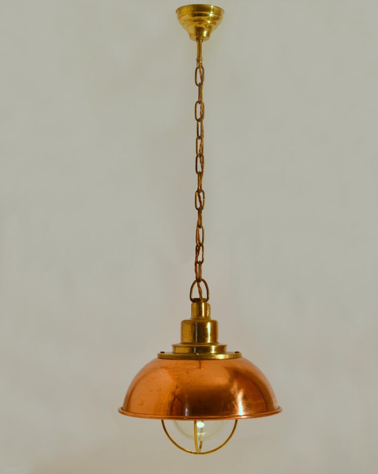 Early 20th century industrial shock-proof pendant in copper and brass with clear glass and brass cage. 
Excellent timeless design of a very functional lamp and beautiful craftsmanship.
Total length with chain and ceiling rose; 85cm.