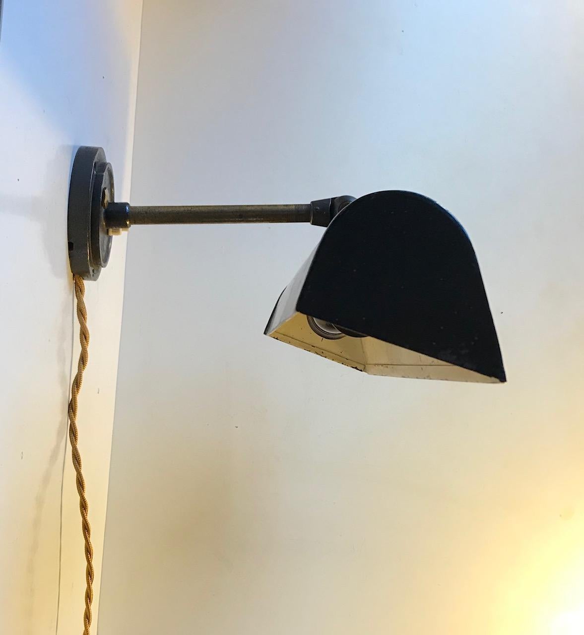 A large wall light with stem and back-plate/mount in brass. It has a wide angled shade in powder-coated steel. The shade is adjustable up/down circa 180 degrees. It features two lightbulbs - E27 up to 75 watts in each. This Industrial looking wall