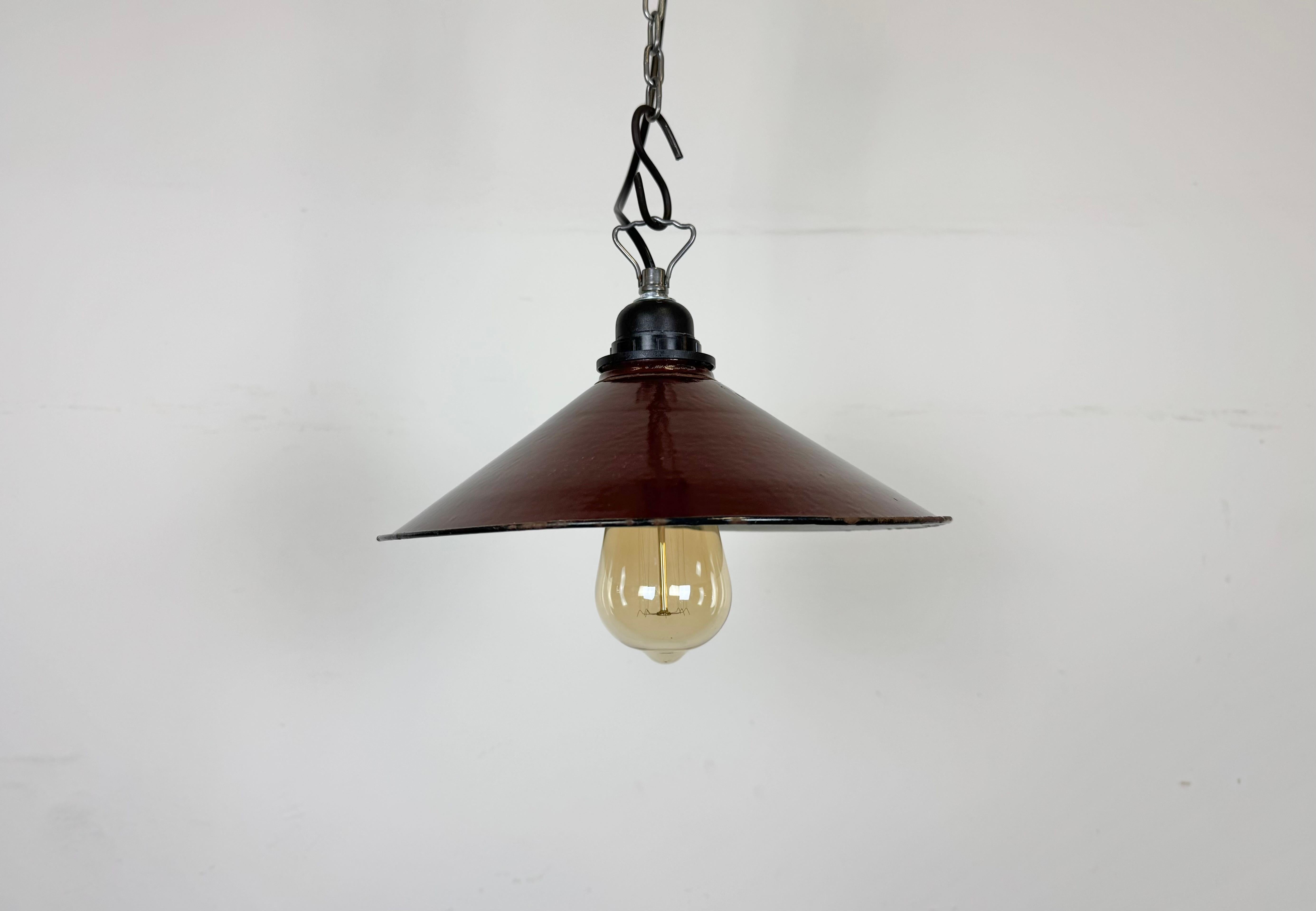 Lampada a sospensione industriale in smalto rosso scuro realizzata in Polonia negli anni Sessanta. Smalto bianco all'interno del paralume. La presa in bachelite con gancio in ferro richiede lampadine standard E 27/ E26. Un nuovo cavo. Completamente