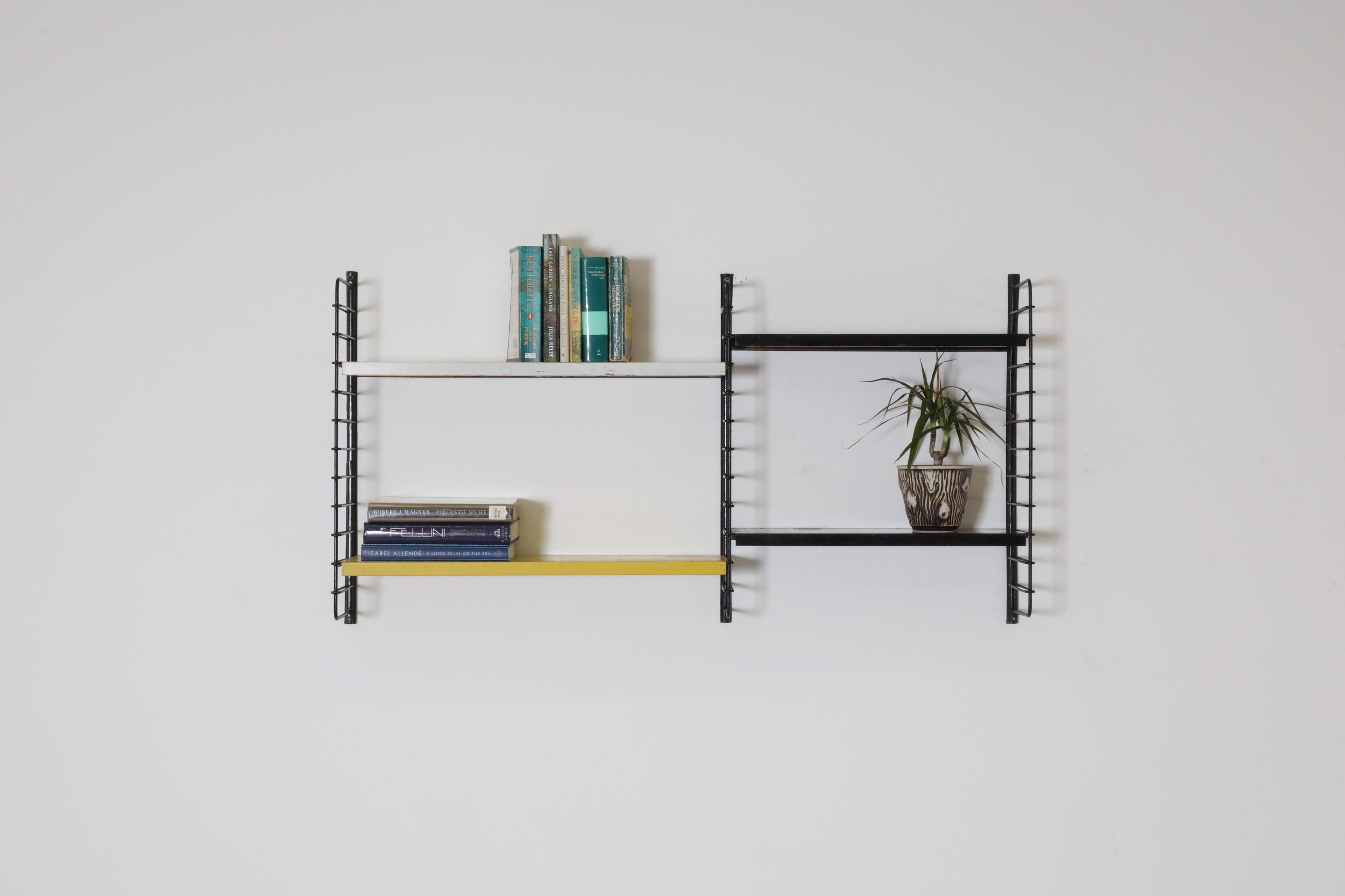 Dutch Mid-Century double section industrial wall mount shelving unit with one wider section, which has a yellow  white shelf and a narrower section with two black shelves. The shelves rest on black enameled metal risers, and all are in very used