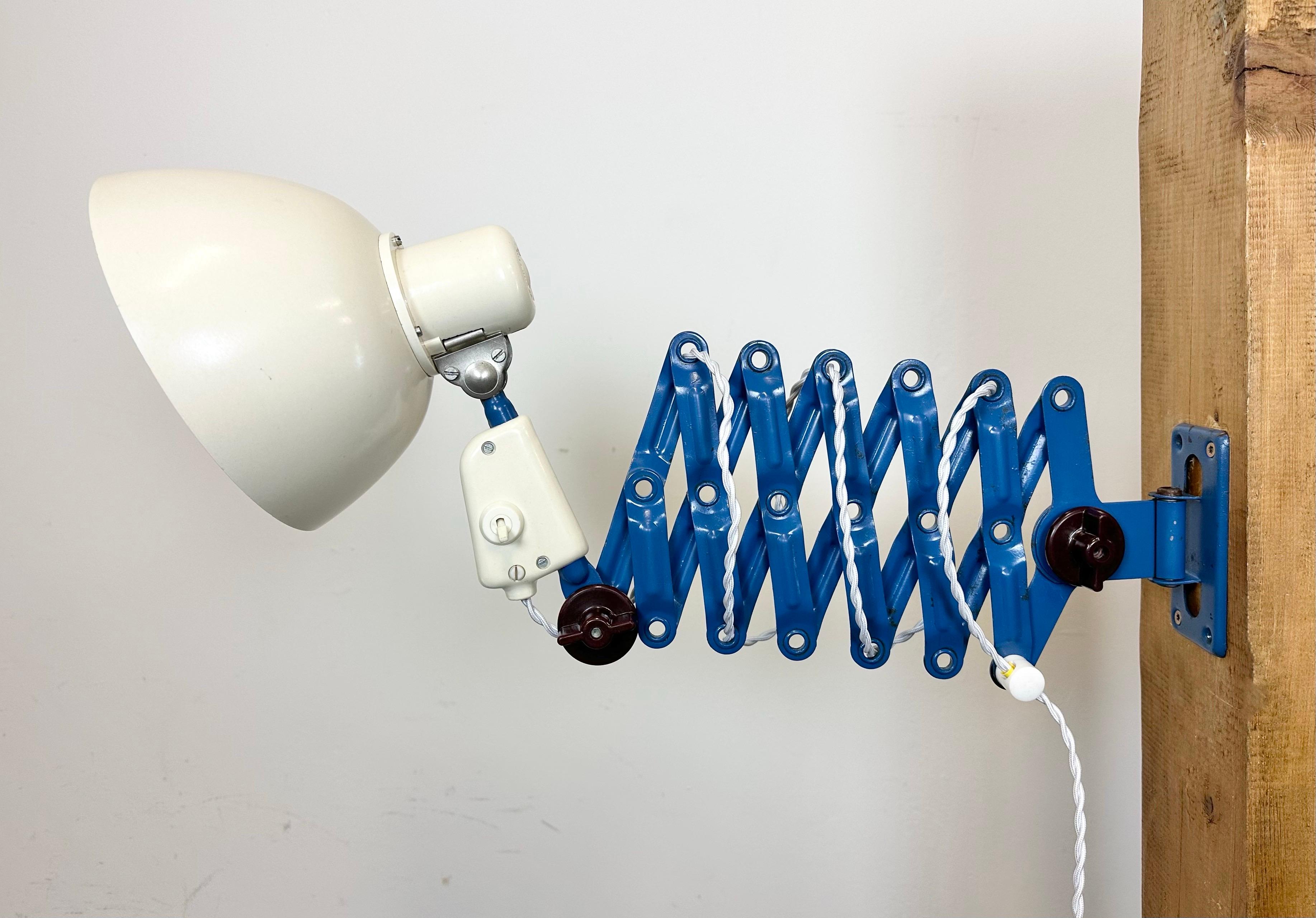 This vintage industrial scissor lamp was produced by VEB ZWECKLEUCHTENBAU DRESDEN in former East Germany during the 1960s. The lamp has a white ( beige ) bakelite shade. A blue iron scissor arm is extendable and can be turned sideways. The original