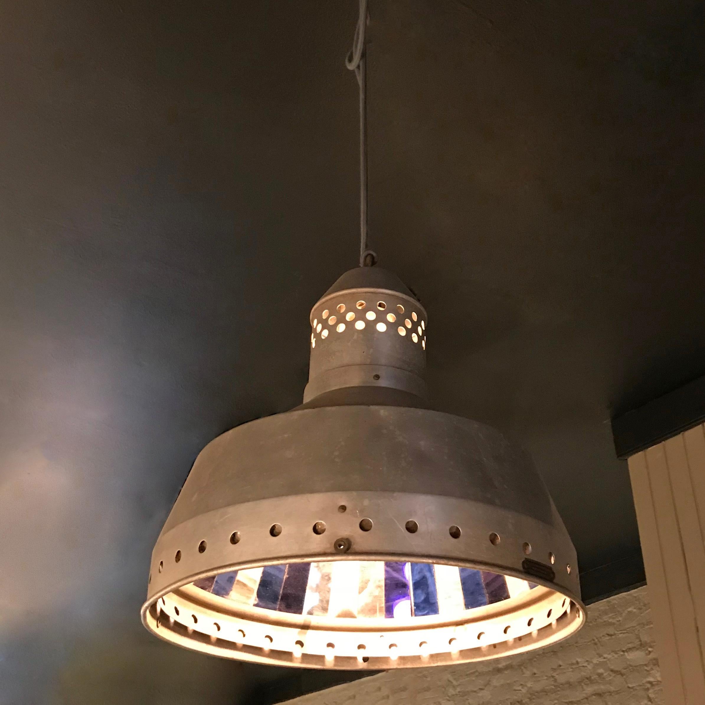 Outstanding, early 20th century, industrial, factory pendant light features a perforated aluminum shade with a faceted mirror interior of alternating blue and clear mirror strips. The pendant is wired with 40 inches of cord to accept up to a 300