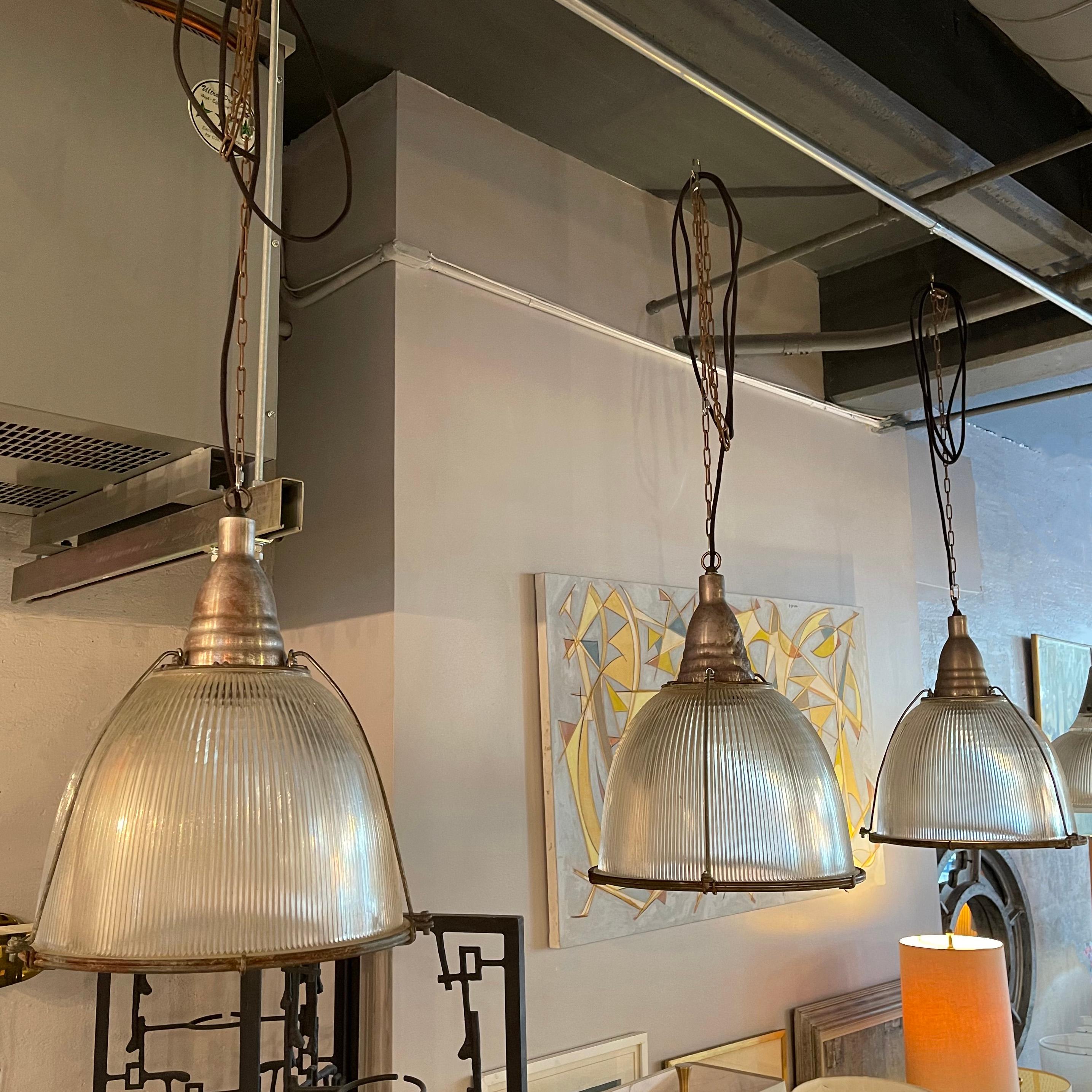 Trio of large, industrial, factory pendants feature Holophane glass dome shades within steel cages with aluminum fitters. The pendants are newly wired with 60 inches of cord on 30 inches of chain. 