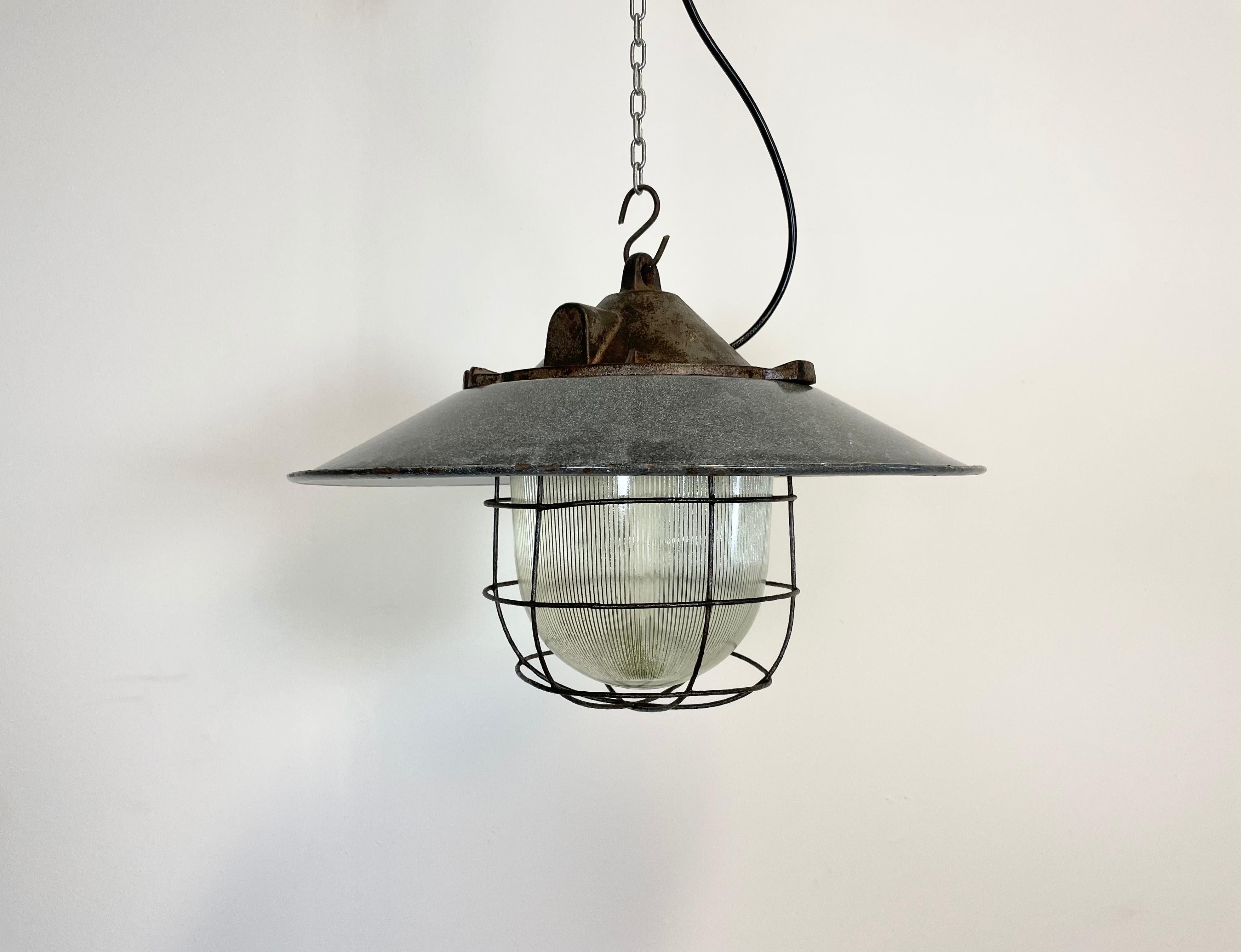 Industrial factory pendant lamp in cast iron made in former Czechoslovakia during the 1950s. It features a grey metal enamel shade with white enamel interior,a striped glass and an iron cage. The porcelain socket requires E 27 light bulbs. New wire.