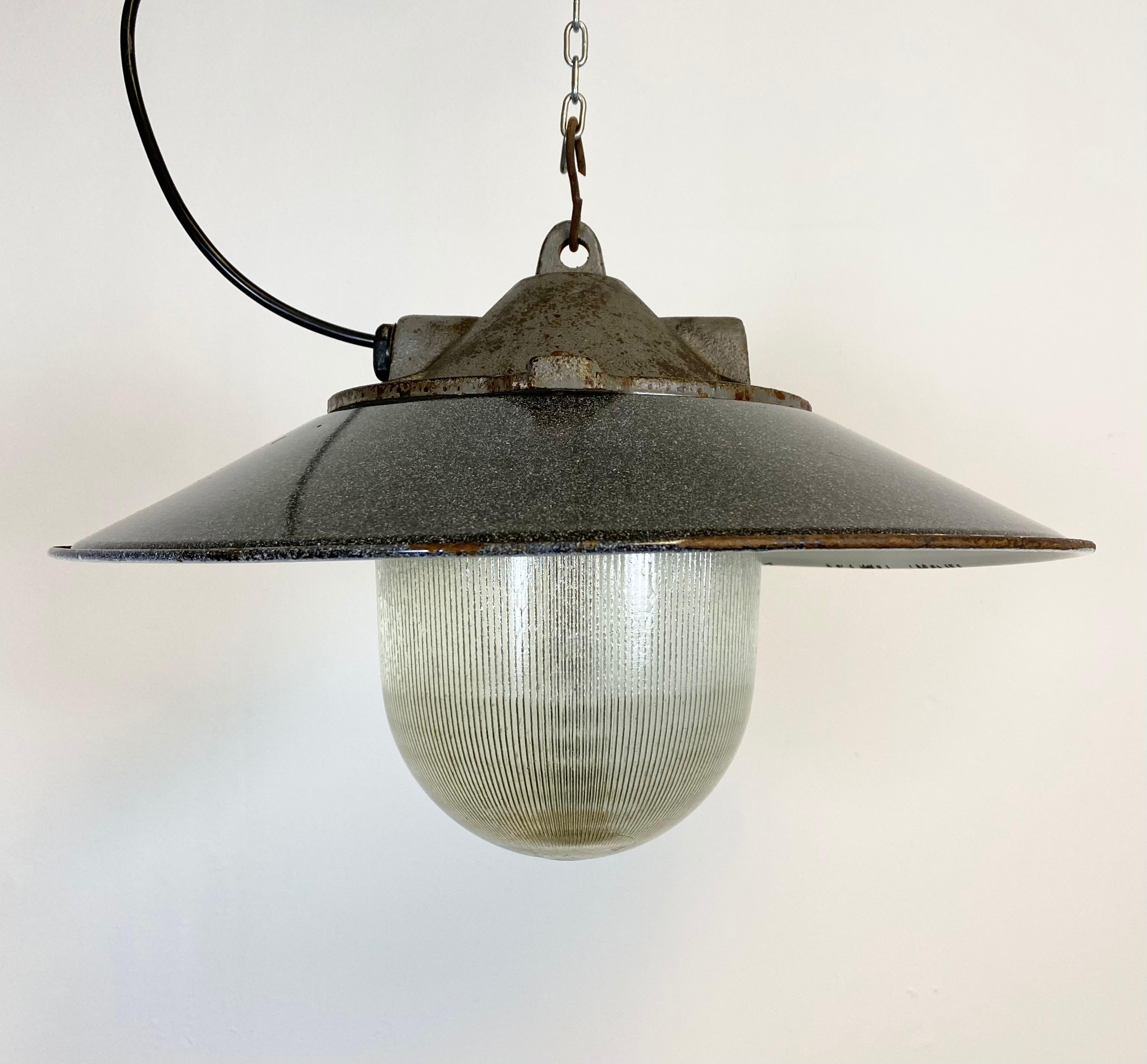 Industrial factory pendant lamp in cast iron made in former Czechoslovakia during the 1950s.It features a grey metal enamel shade with white interior. Striped glass. Porcelain socket for E 27 light bulbs. New wire. The weight of the lamp is 6.0 kg.