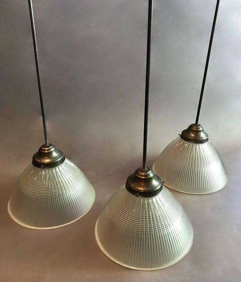 Industrial, factory pendant lights feature deeply cut, prismatic, Holophane glass, dome shaped shades with steel fitters, long stems and canopies. Measure: Height of the pendants with the stems is 45 inches. The height of the shades with fitters is